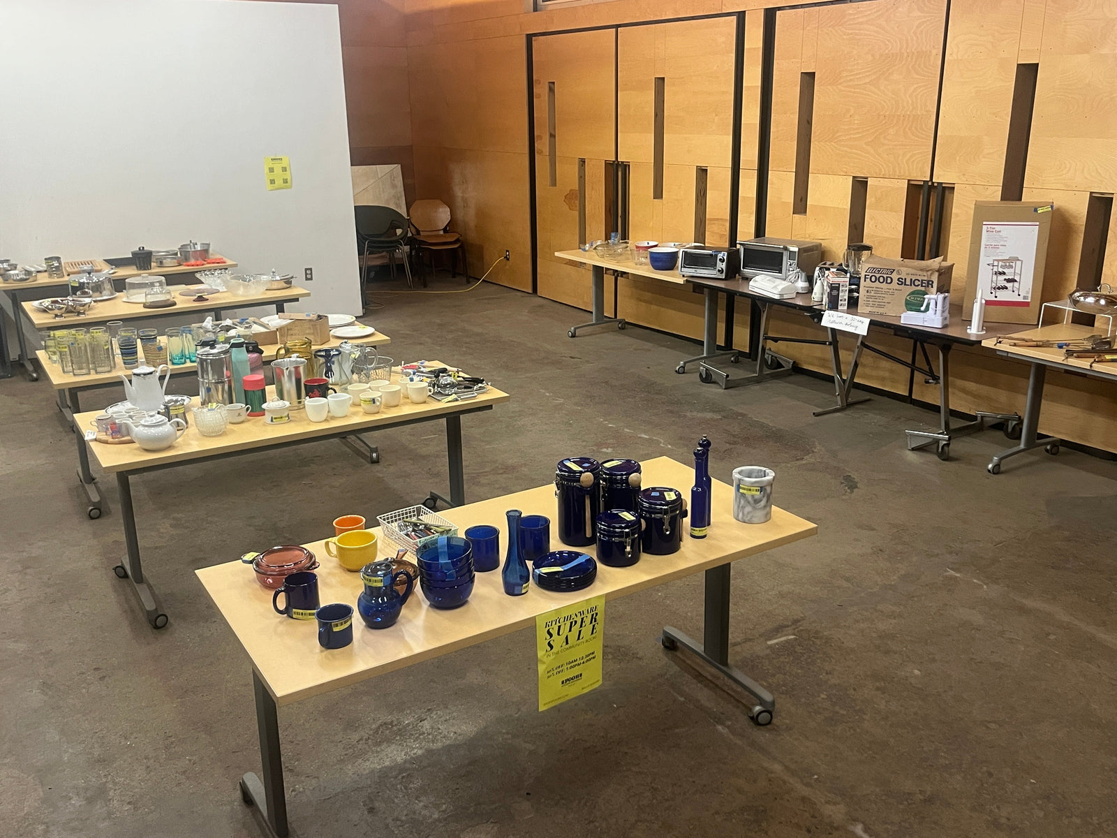 Kitchenware products are arranged on rows of wood conference tables in Construction Junction's Community Room