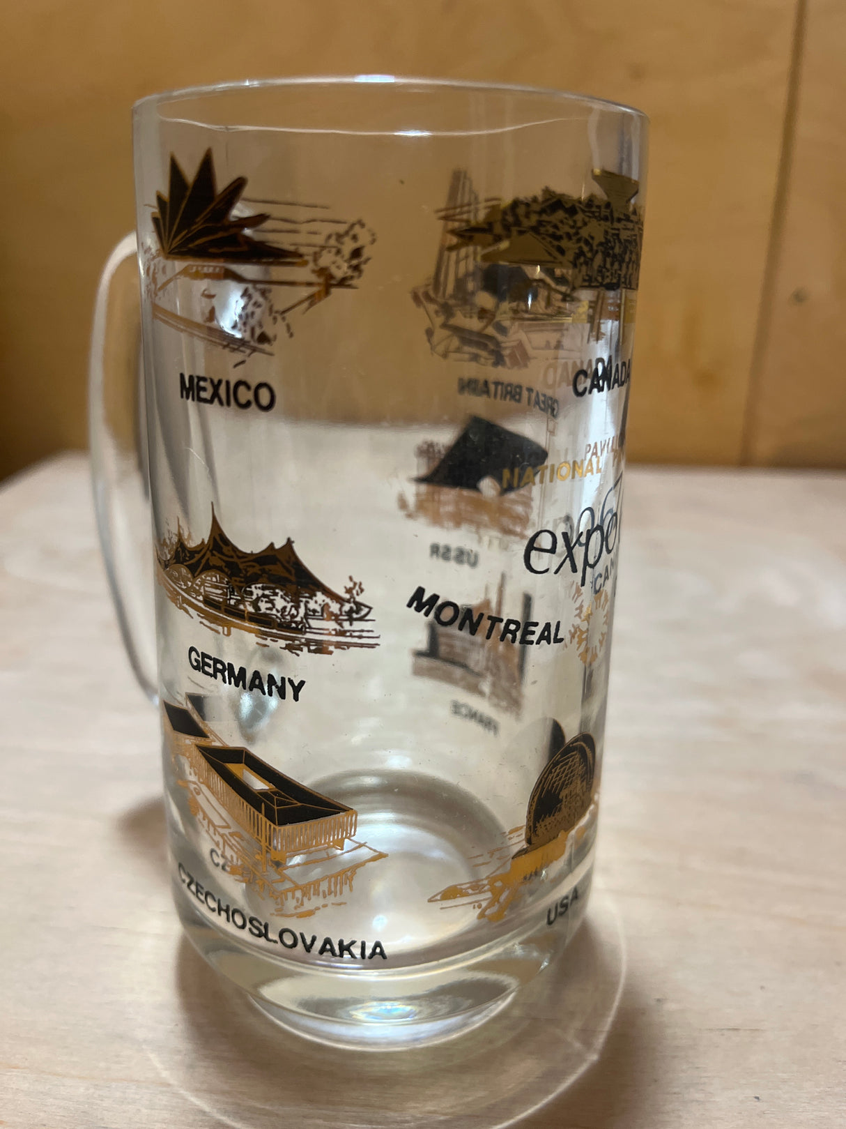 EXPO 1968 Souvenir mug featuring gold and black illustrations of international pavilions and names from Expo 67, including the USA's geodesic dome and official logo.