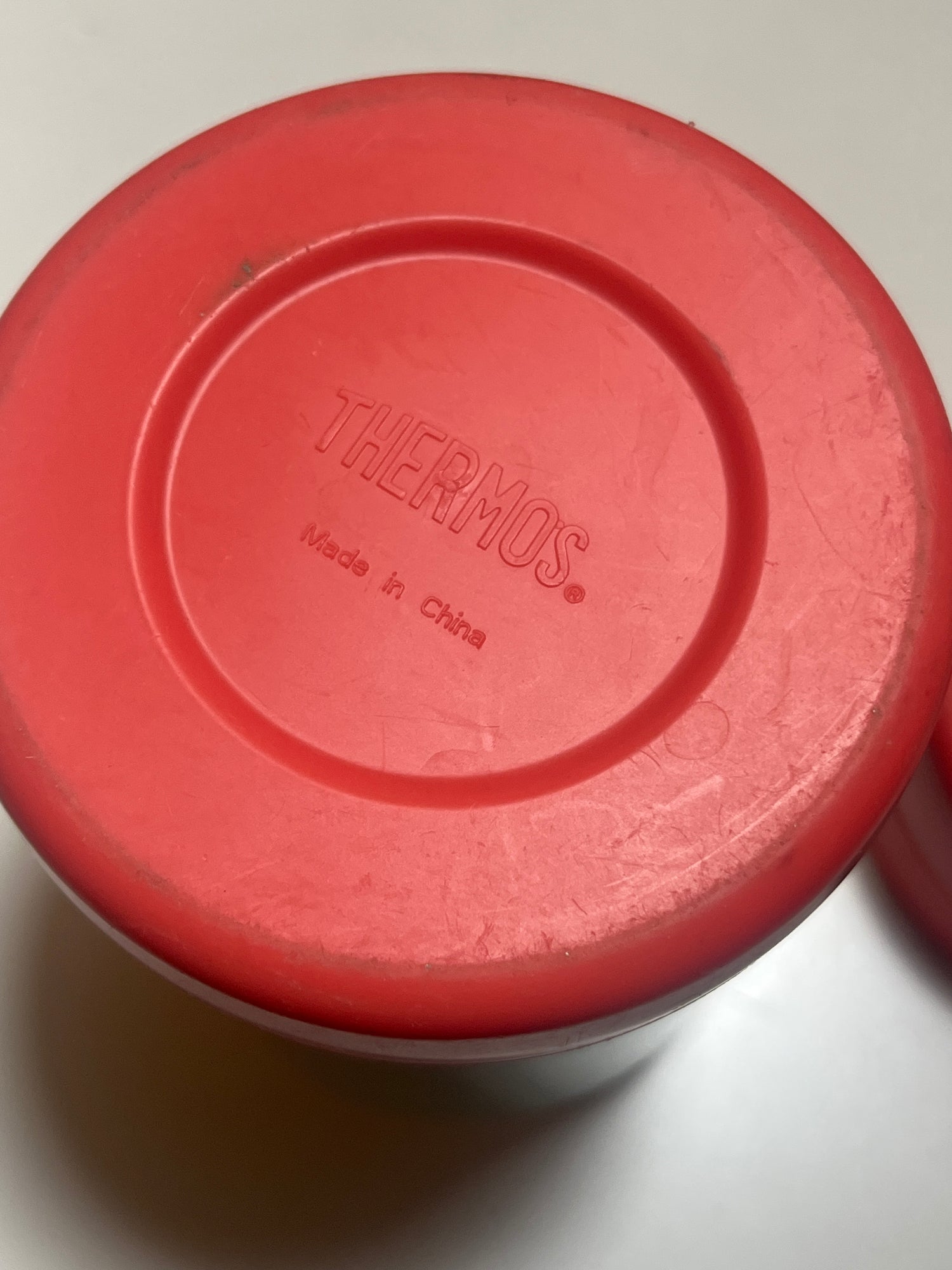 Double-walled pink and green Thermos, ideal for keeping meals warm, features a red lid, resembling a frisbee, placed on a white surface.