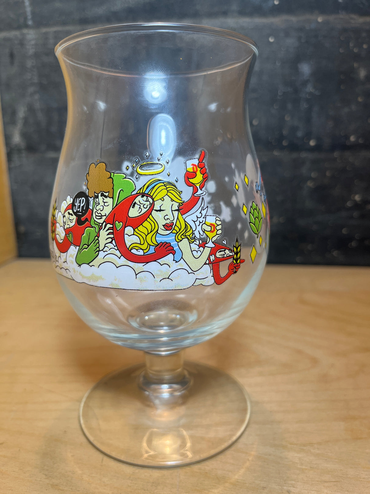 Huvel Belgian beer glass with limited edition 2024 JT Samuels illustration featuring an angel, noodle-like creatures, hop cones, and wheat stalks on its bowl.