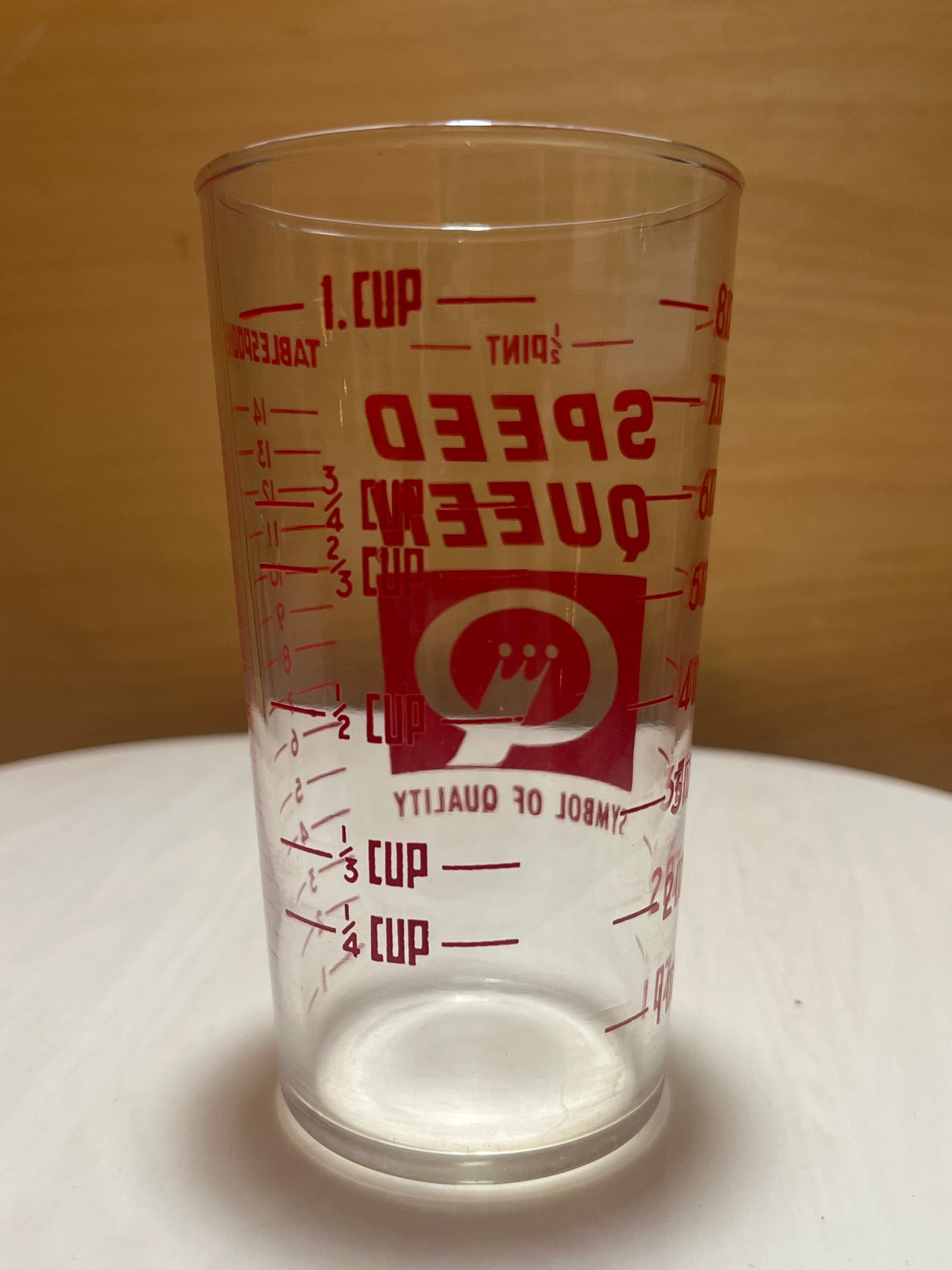 Speed Queen glass measuring cup with clear plastic design, featuring red volume markings and logo, displayed empty on a plain surface.