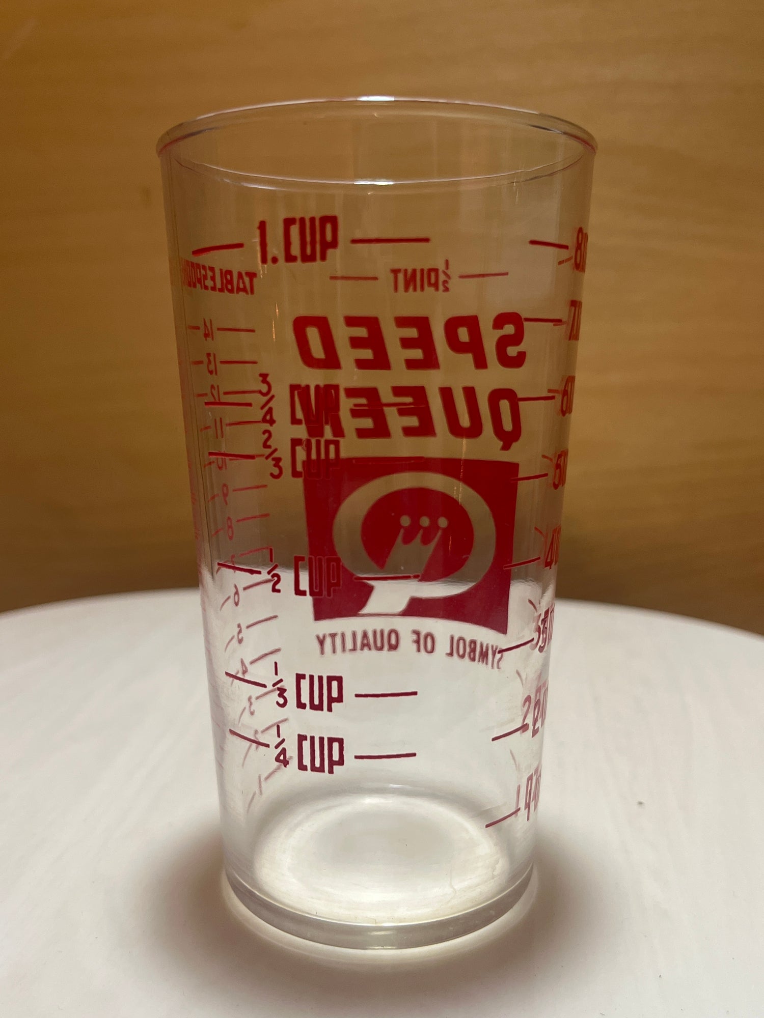 Speed Queen glass measuring cup with clear plastic design, featuring red volume markings and logo, displayed empty on a plain surface.