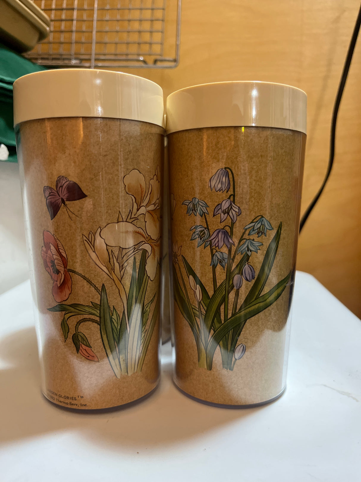 Thermo-Serv set of 4 insulated plastic mugs featuring floral illustrations, perfect for outdoor dining, shown close-up near a vase and table setting.