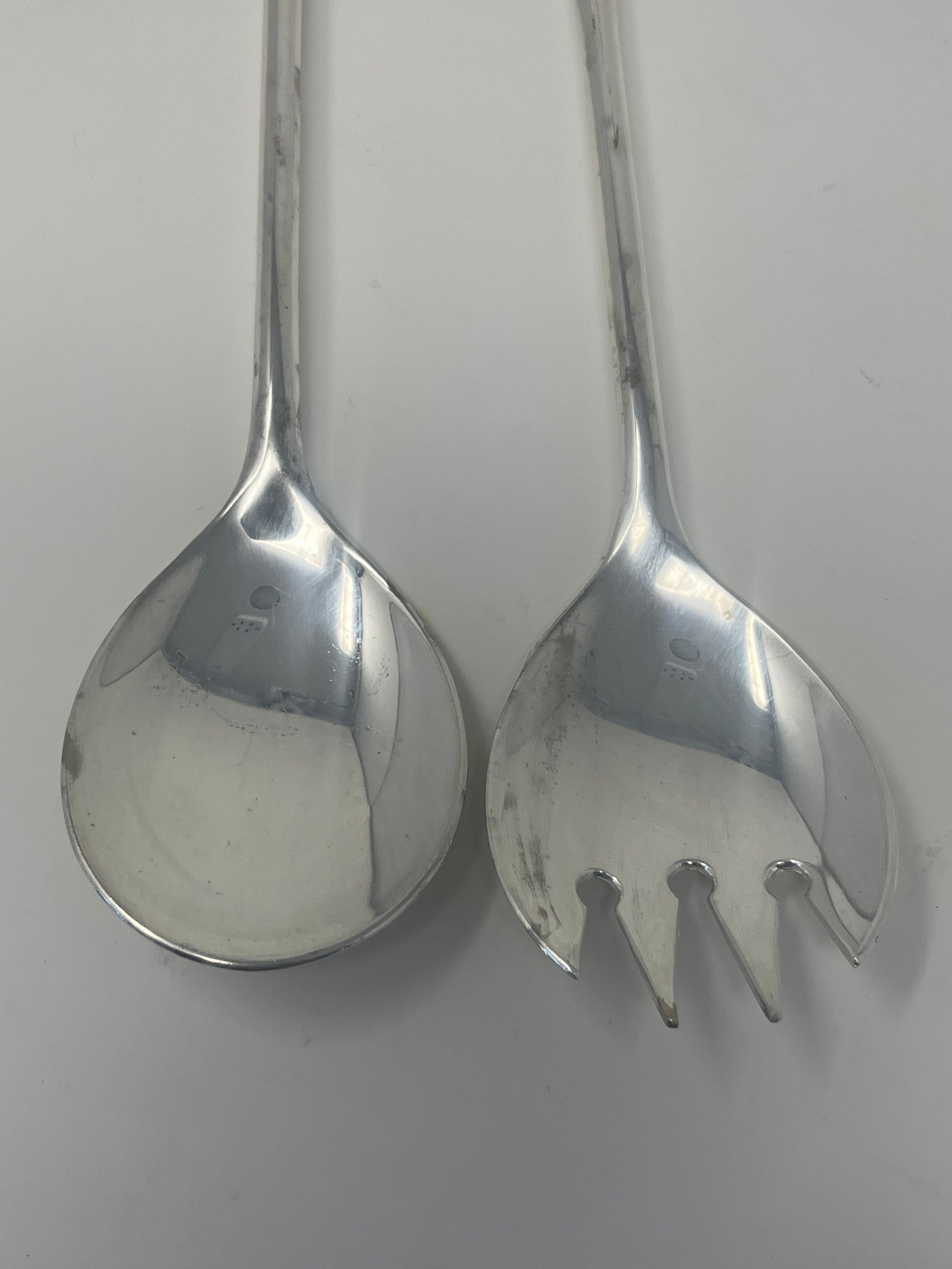 Italian silver plated salad tongs with an elegant, minimalist design, visible tarnish from use, displayed on a white surface. Made in the 1970s.
