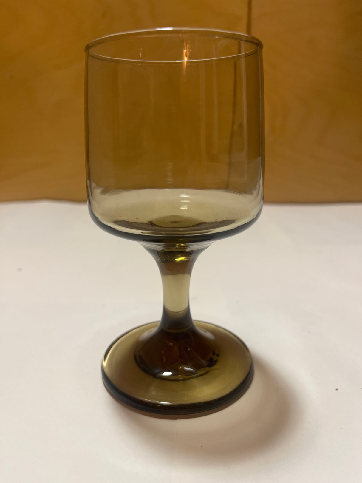 Libbey Tawney wine glass, a single amber-tinted goblet with a stem, displayed on a white surface, set against a warm wooden backdrop.