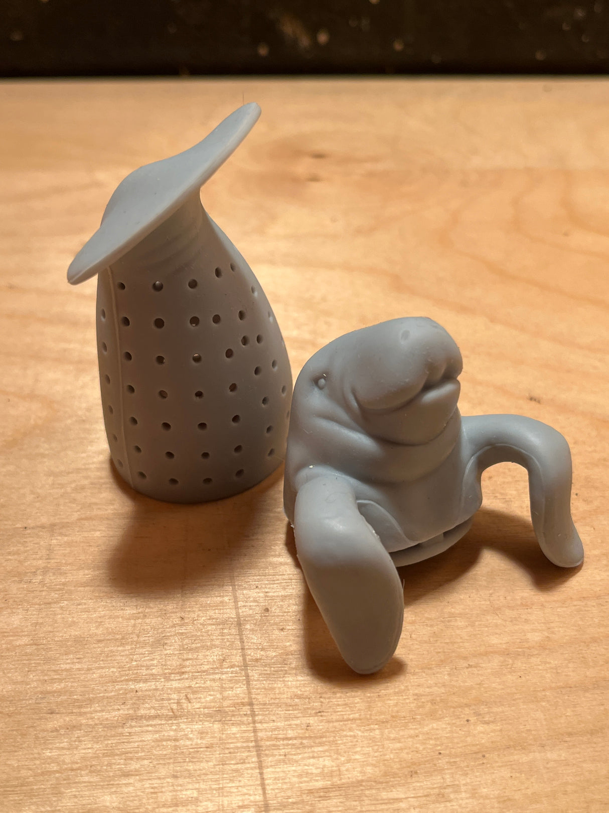 ManaTea infuser on wooden surface, featuring a perforated steeping chamber and manatee-shaped cap. Crafted from food-safe silicone for adorable, efficient tea brewing.
