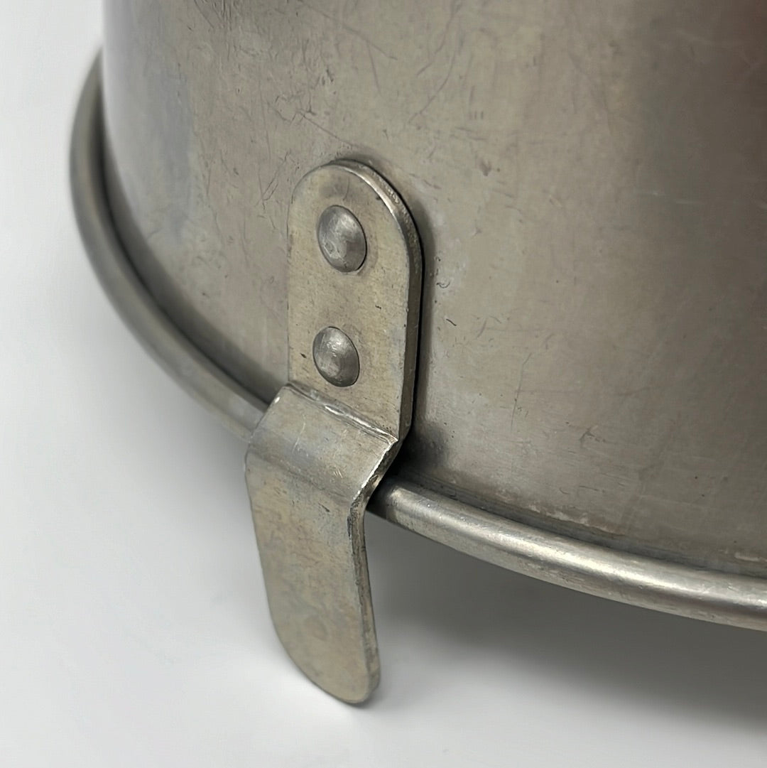 Close-up of a Mirro 5533M Angel Food Cake Pan with Cooling Feet, a riveted handle attachment, a worn surface, and spoons in the kitchen exchange.