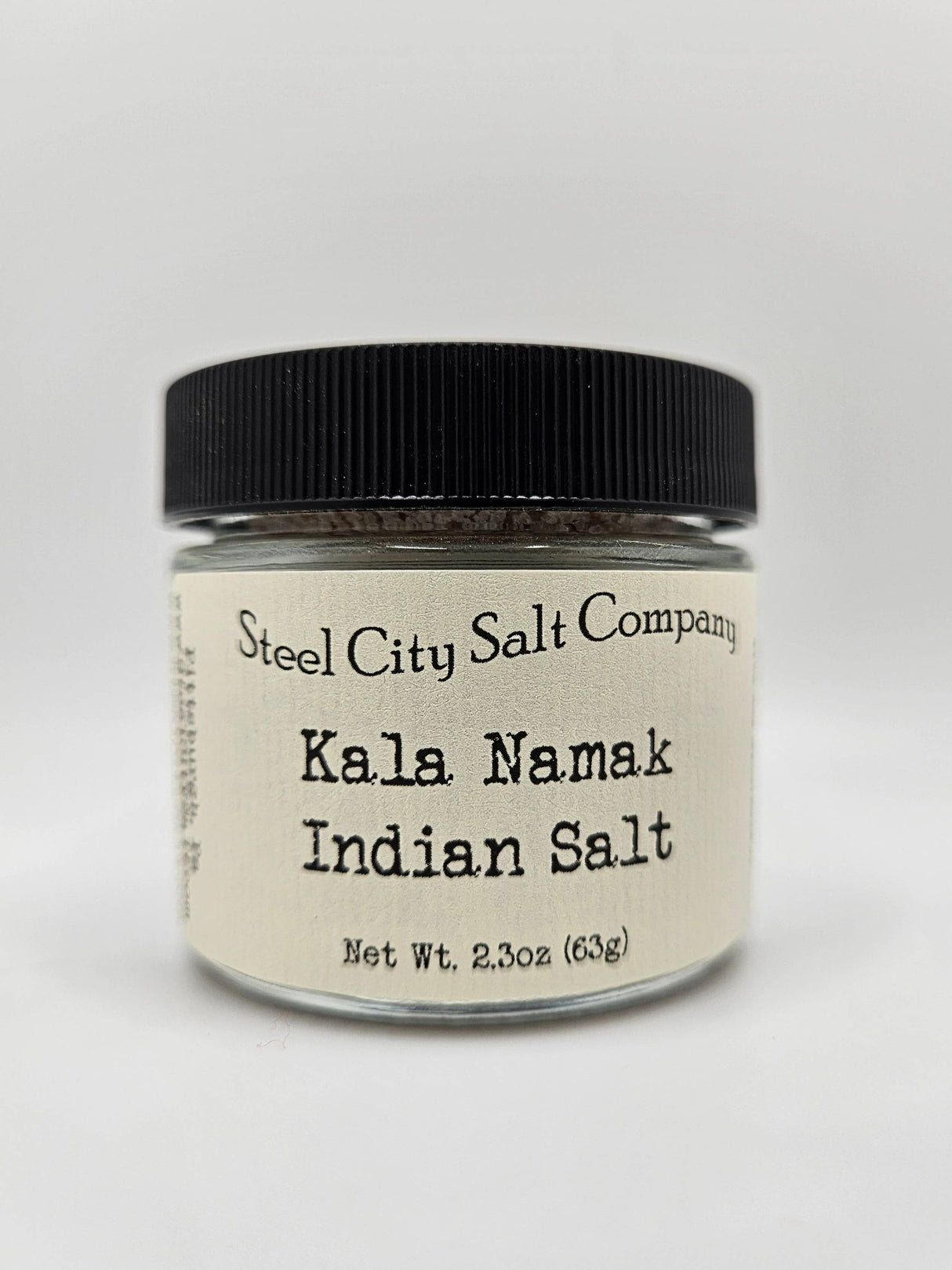 Kala Namak Indian Salt in a 2.3 oz glass jar with a black lid and cream label, known for its egg-like flavor, ideal for vegan cooking.
