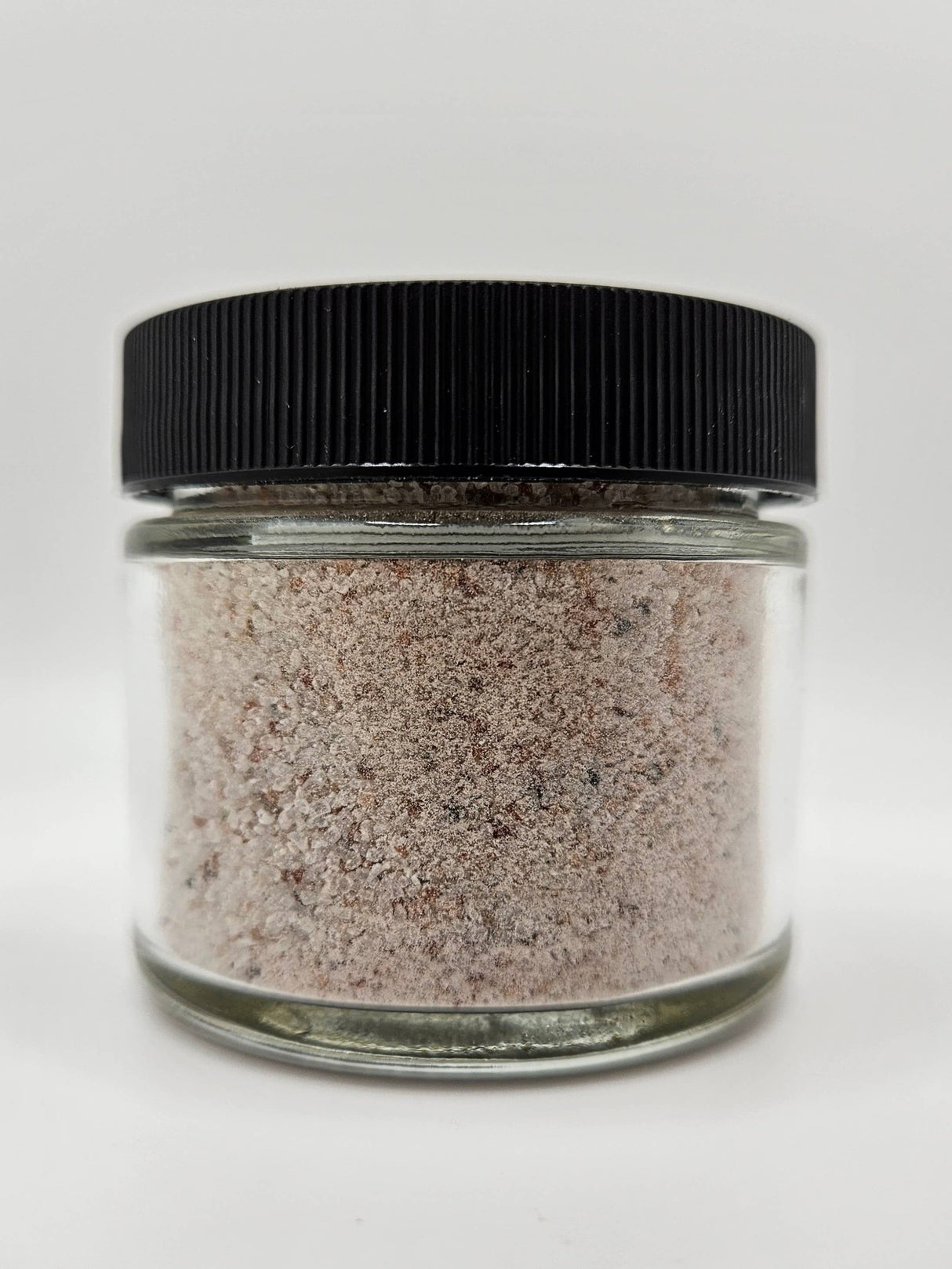 Kala Namak Indian Salt in a clear jar with black lid, showcasing its pinkish-gray granules, known for its egg-like flavor, ideal for vegan cooking.