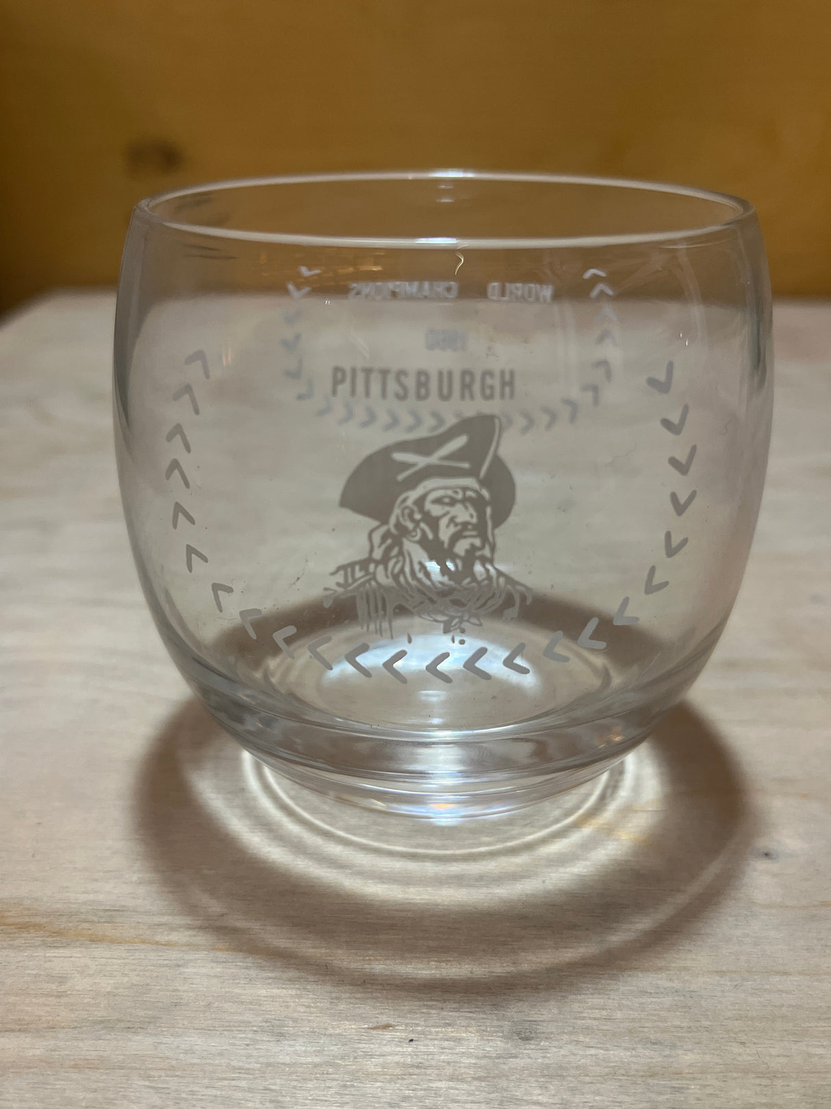 RARE 1960 Pittsburgh Pirates World Champions commemorative drinking glass with PITTSBURGH and pirate head illustration on wooden surface.