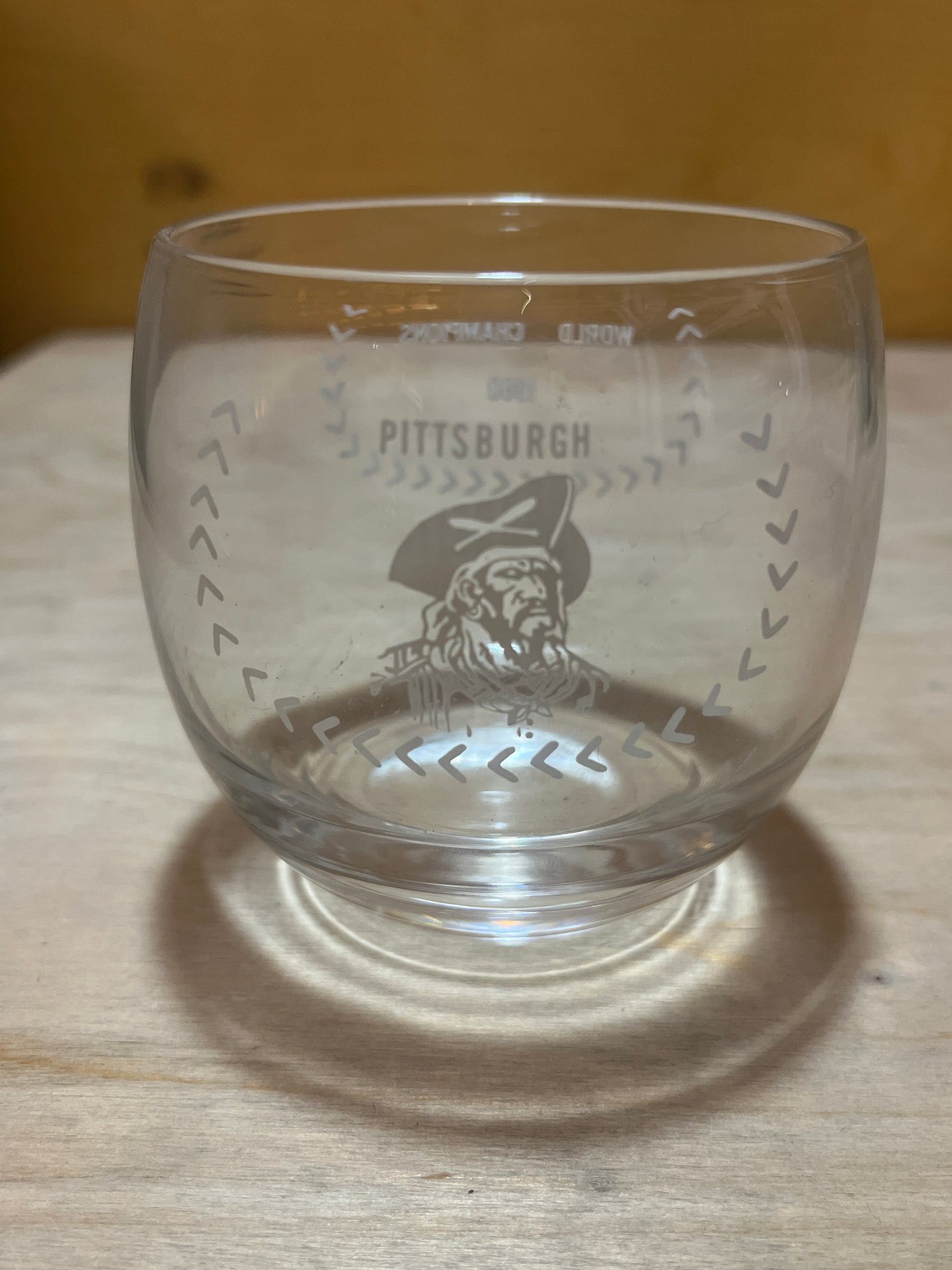 RARE 1960 Pittsburgh Pirates World Champions commemorative drinking glass with PITTSBURGH and pirate head illustration on wooden surface.
