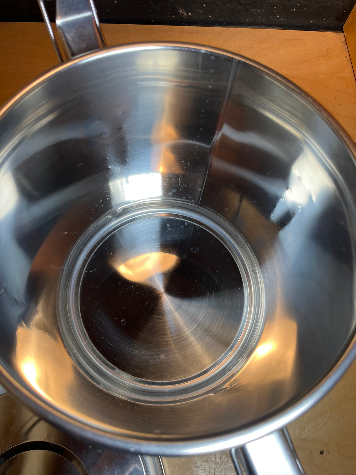 Stainless steel food storage container with clasps, handle, and silicone seal, shown open with reflective interior on wooden countertop, highlighting its spacious, durable design.