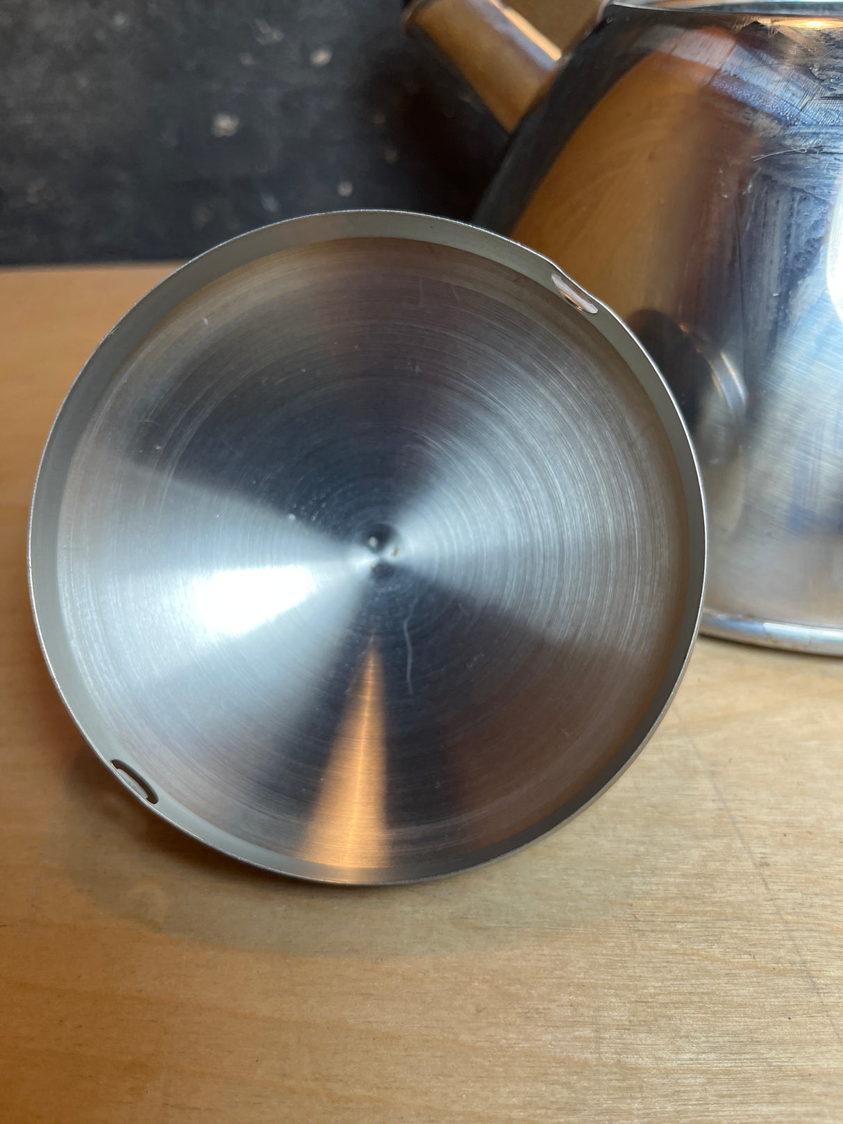 Farberware 2.5-quart whistling tea kettle, featuring a stainless steel lid with machined concentric ridges and notches, shown with a black handle and red accents.