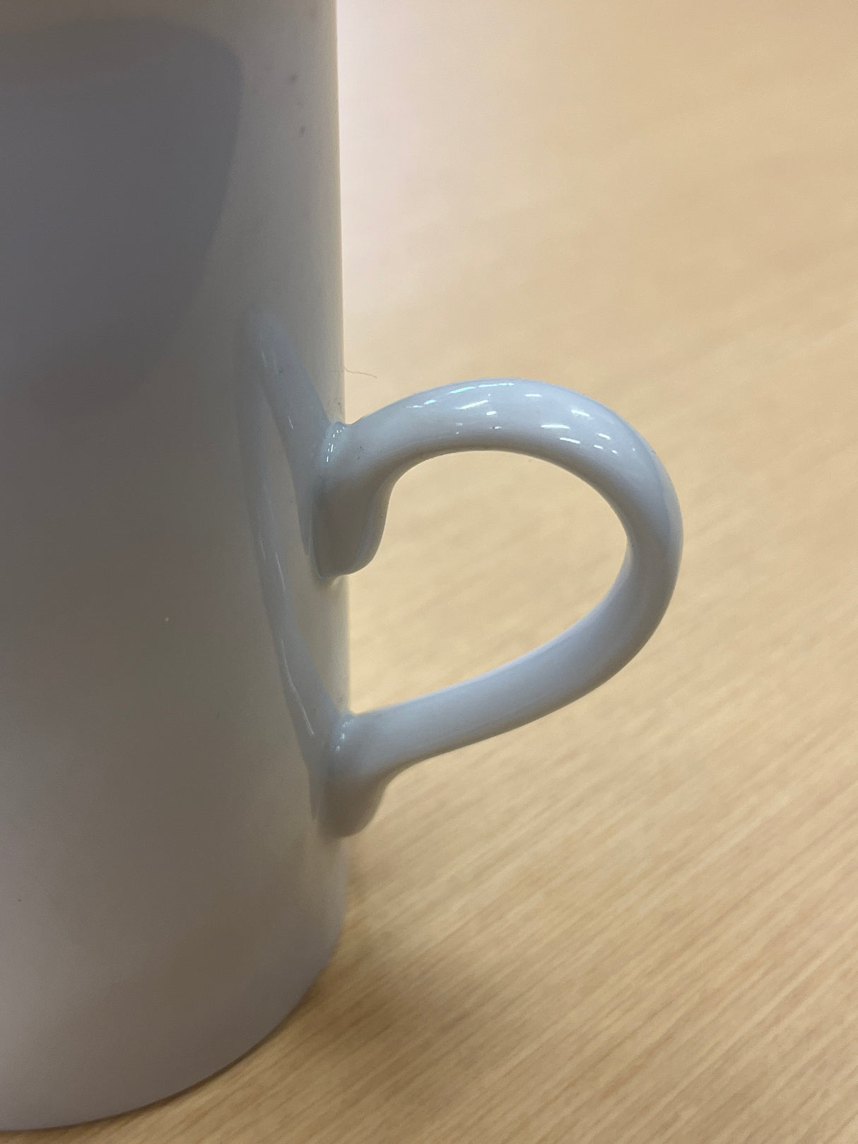 Close-up of tall ceramic white coffee mug with delicate, modern handle, showcasing its elegant design and smooth glaze. Part of an everyday coffee mug set.