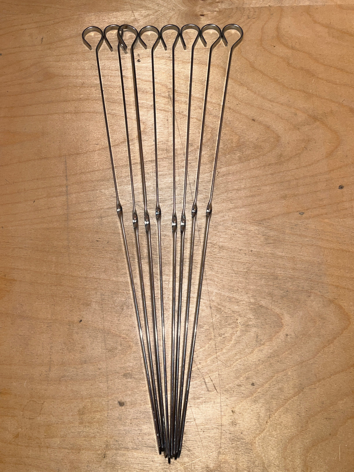 Food skewers - set of 8 reusable 14” stainless steel, featuring looped handles and pointed tips, laid out on wood, ideal for grilling or broiling.