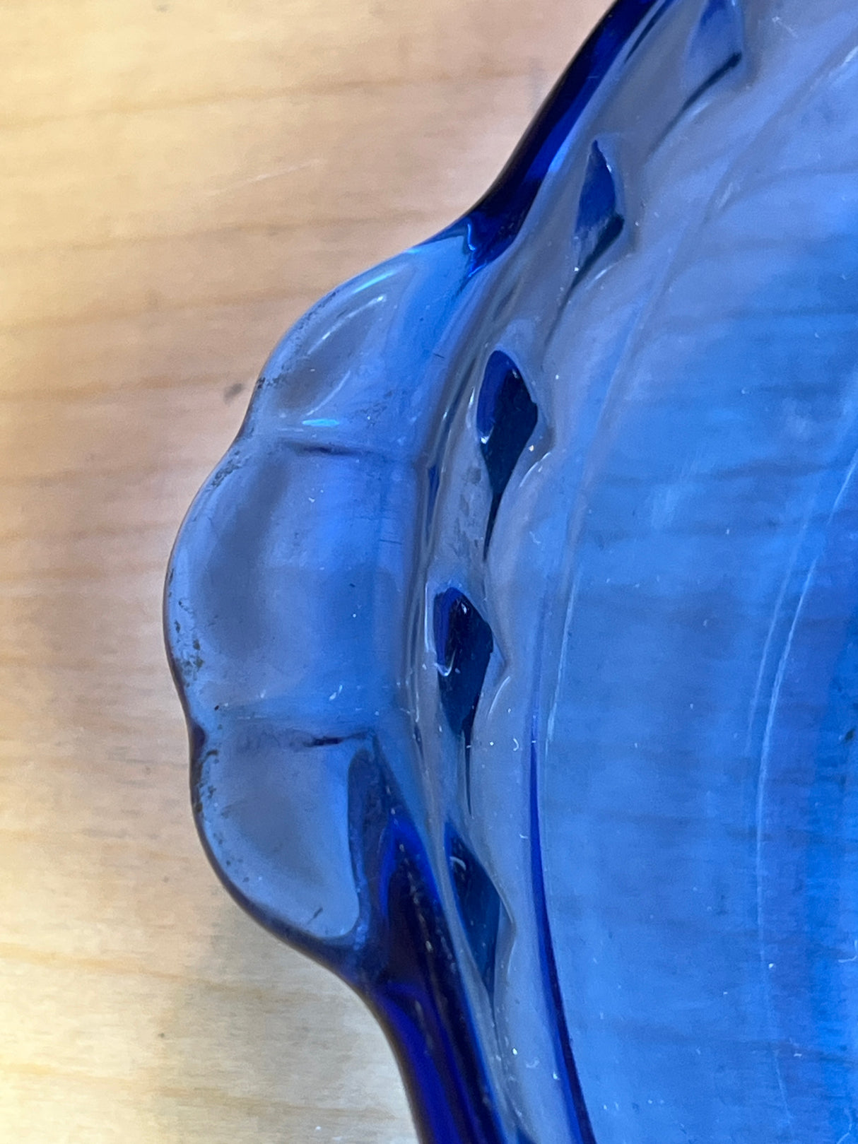 Close-up of Pyrex 229 cobalt blue glass pie/casserole dish with fluted edges, highlighting its scalloped rim on a wooden tabletop.
