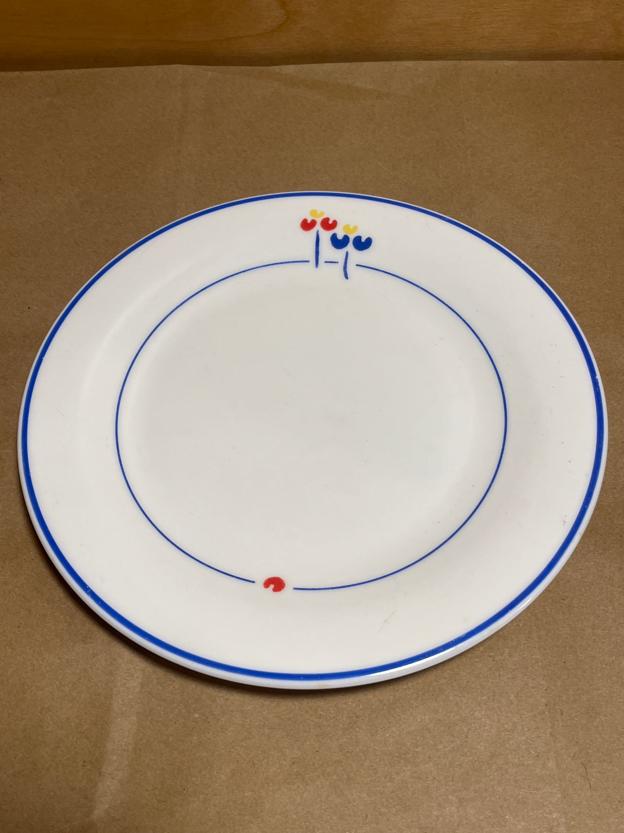 Rival Designs Tulip dinnerware collection Lot 3078 features a white ceramic plate with blue rings and stylized flower accents, embodying elegant simplicity.