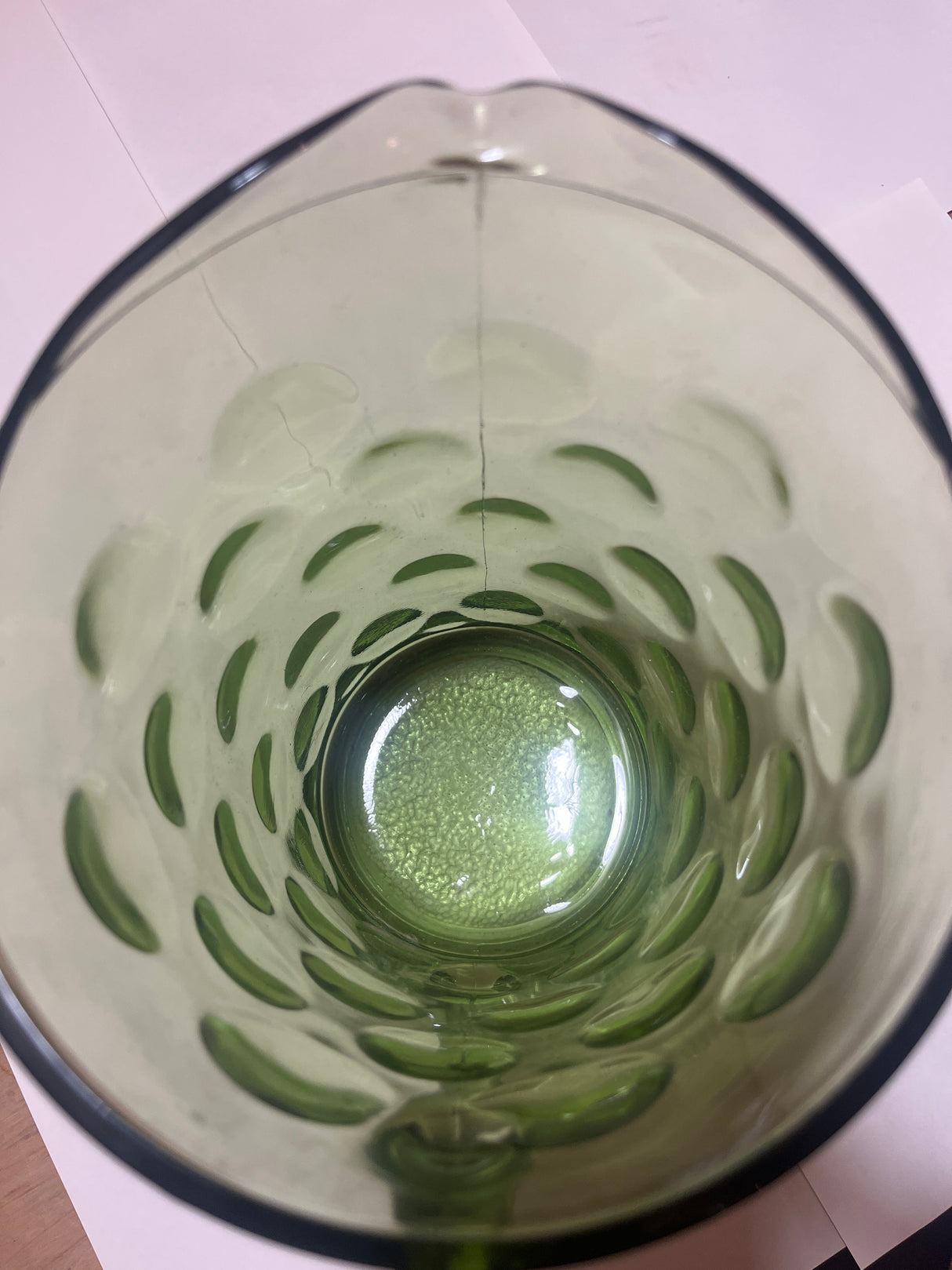 Looking down into the Hazel Atlas Eldorado avocado green coin dot glass pitcher, showcasing its bubble-patterned interior with slight liquid and resting on white paper.