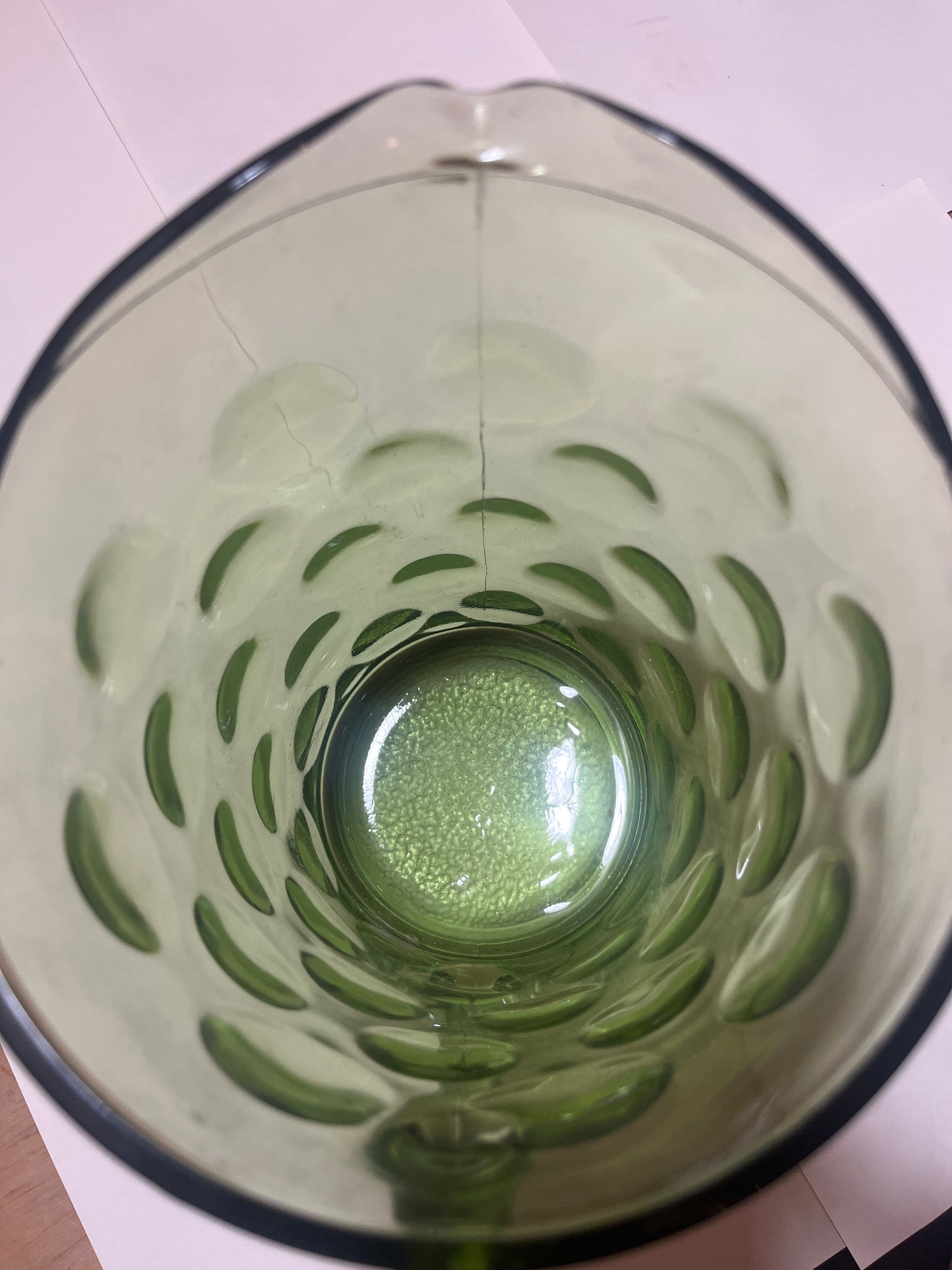 Looking down into the Hazel Atlas Eldorado avocado green coin dot glass pitcher, showcasing its bubble-patterned interior with slight liquid and resting on white paper.
