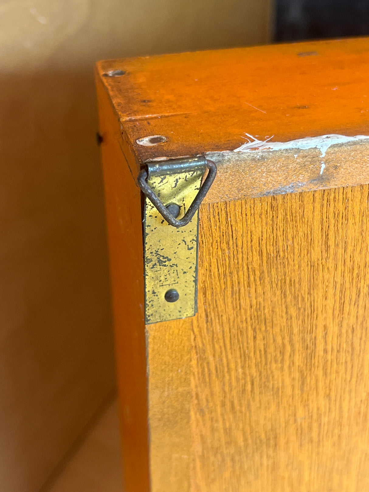 Close-up of a Funky floral wooden spice rack's back corner, highlighting its wood grain, orange top edge, and brass D-ring hanger for wall mounting.