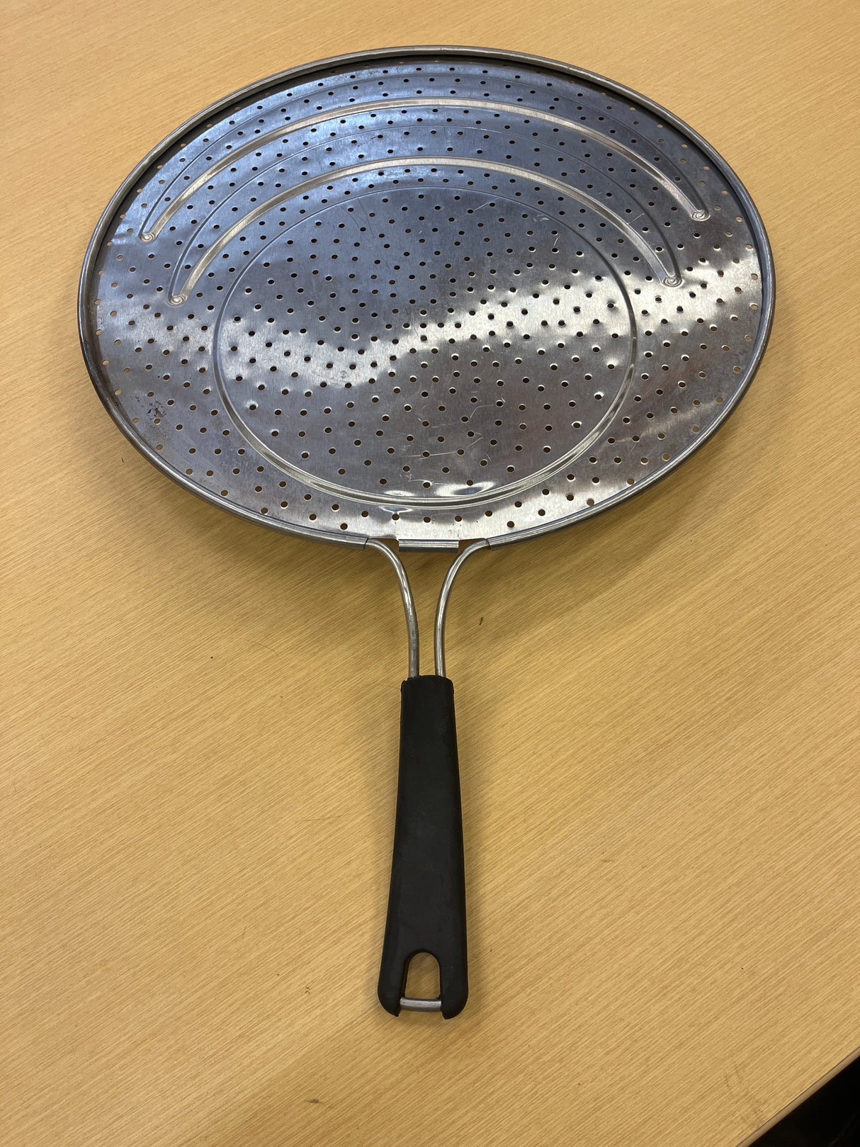 Calphalon 13 stainless steel splatter guard with silicone lined handle, designed to fit pans 8-12, shown on a wood surface with metal plate detail.