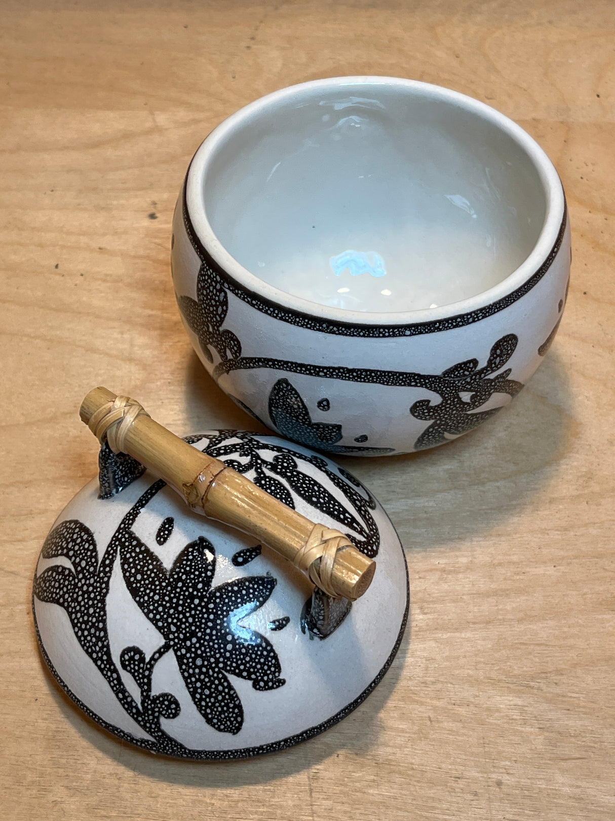 Set of 8 white mugs and sugar bowl with lid featuring a black dotted floral-vine pattern and bamboo handle on a light wood surface.