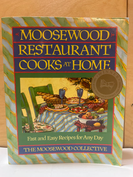 Cover of the cookbook Moosewood Restaurant Cooks at Home featuring a dining table scene, with a James Beard Award seal in the corner.