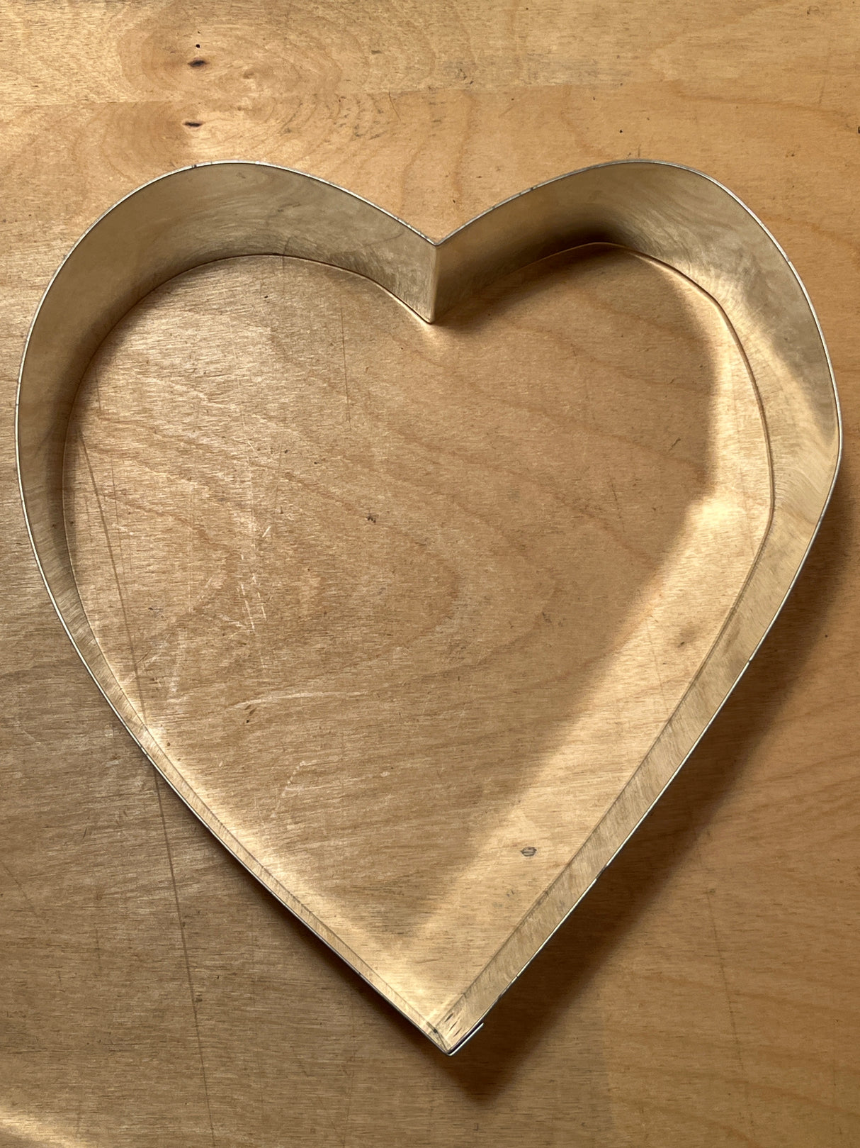 Heart-shaped metal pastry cutter on wooden board, part of the 4-piece springform pan set by Pampered Chef, ideal for baking and crafting.