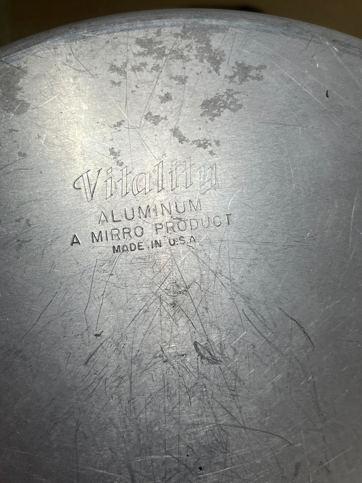 Close-up of a worn aluminum surface stamped with Vitality from a Set of 4 Aluminum Vitality by Mirro four-tier wedding cake pans, showcasing vintage craftsmanship.