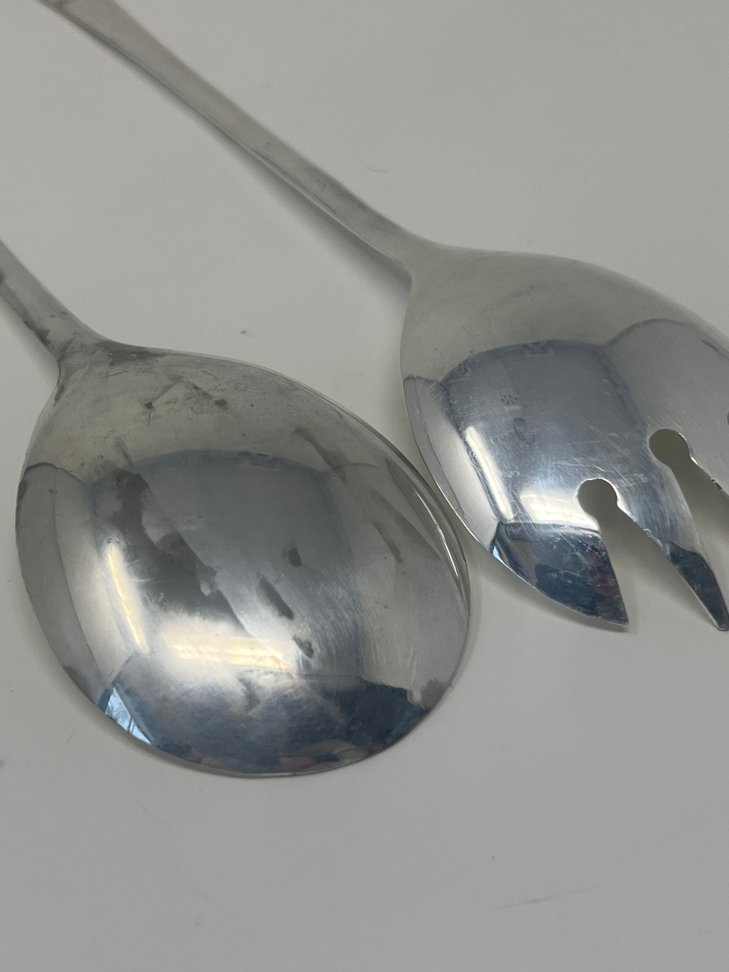 Italian silver plated salad tongs with a minimalist design, featuring a distinct hole in the spoon, displaying slight tarnish typical of vintage 1970s pieces.