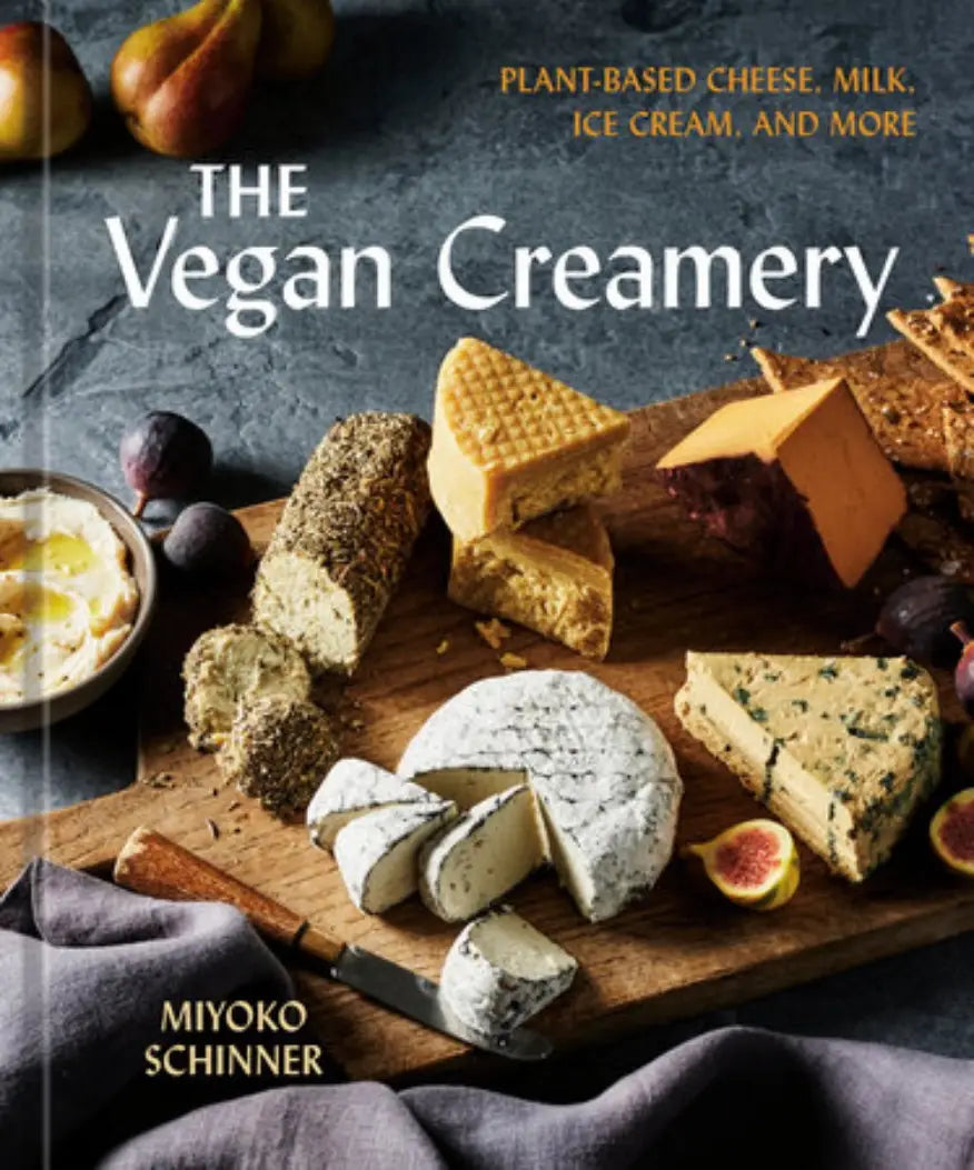 Cover of The Vegan Creamery cookbook featuring assorted homemade vegan cheeses on a wooden board with figs, pears, crackers, and a cheese knife.