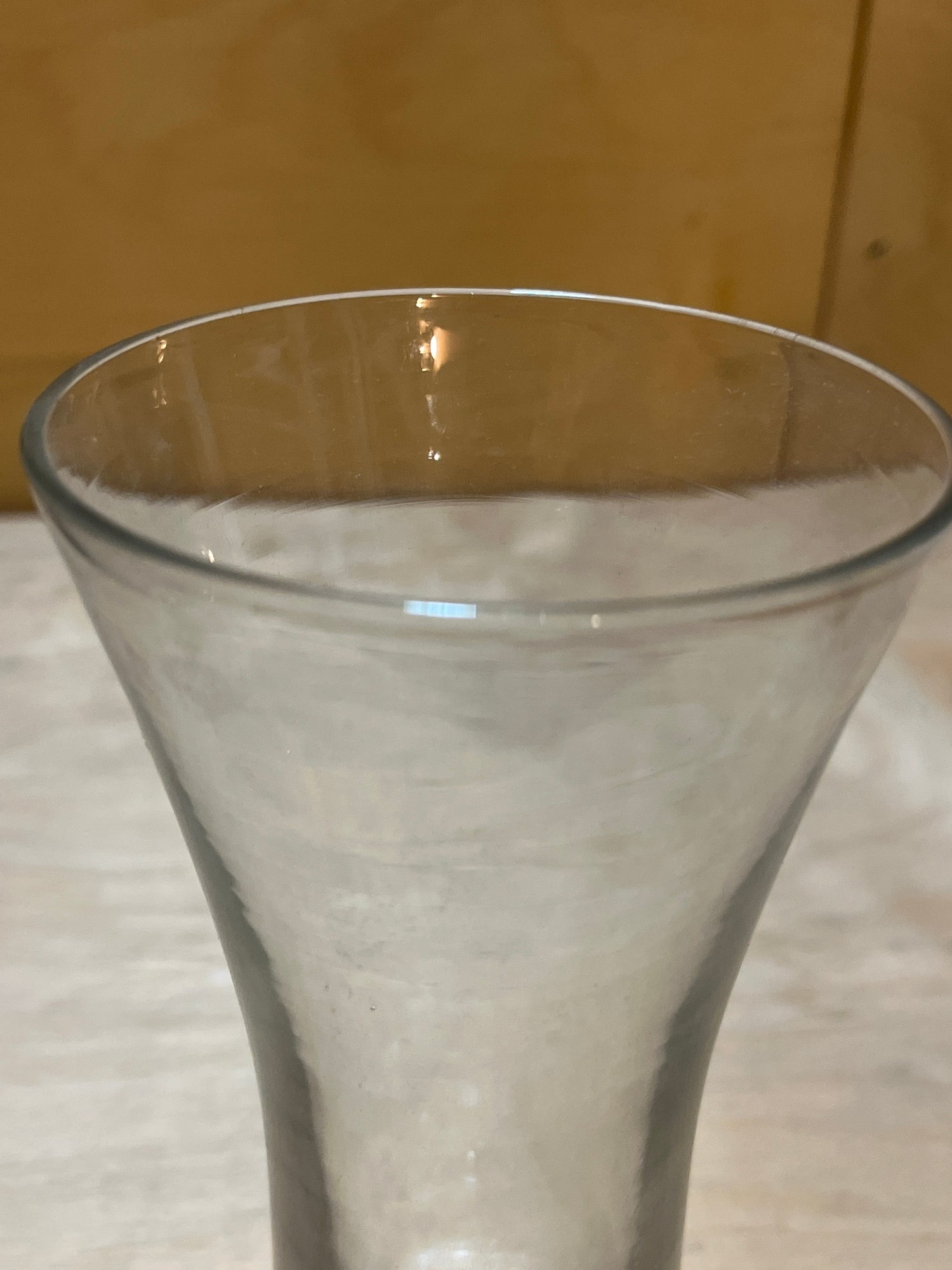 Tall Pilsner beer glass with gently flared sides, a wider opening at the top, and a sturdy weighted base, sitting on a light surface.