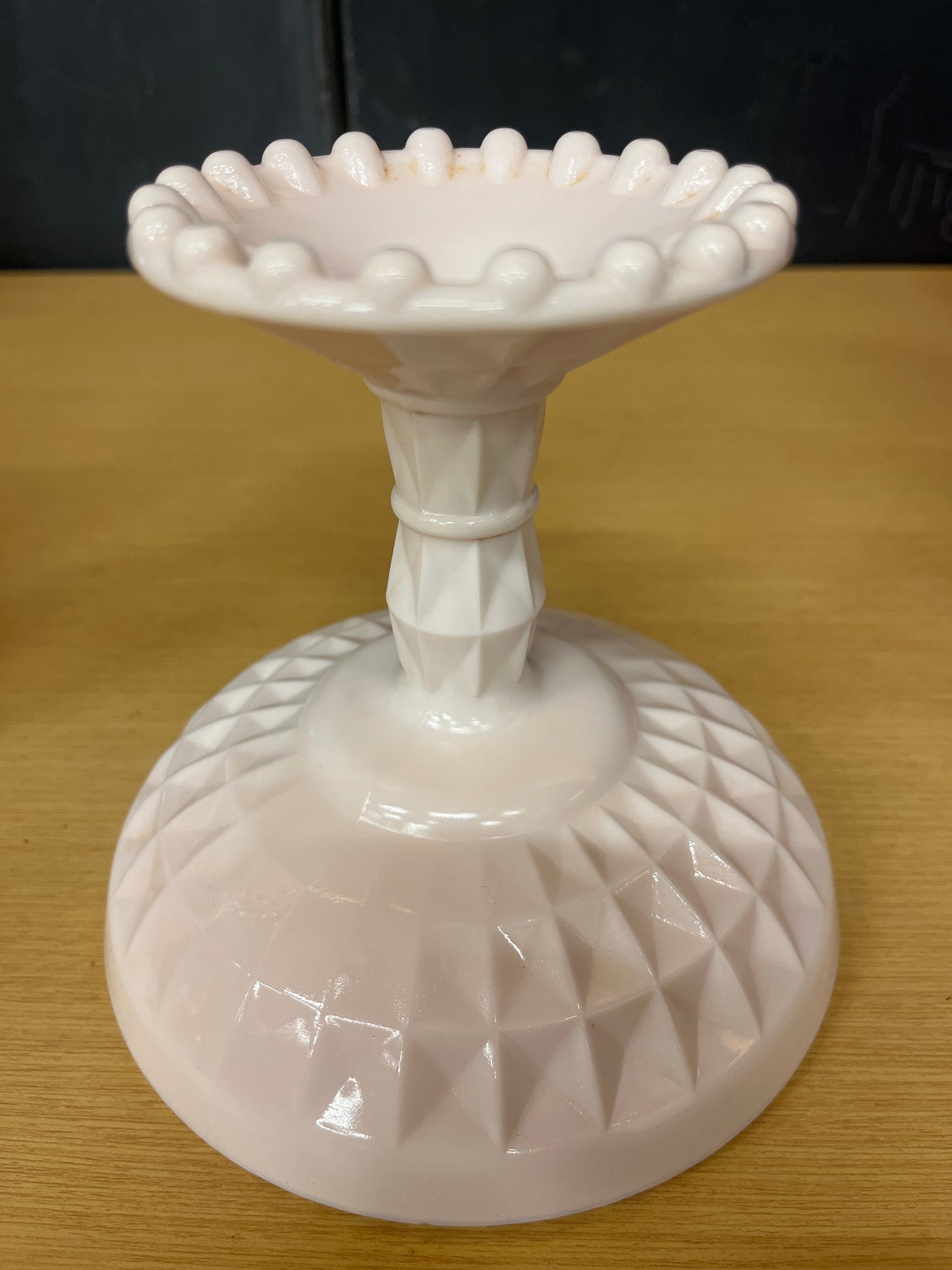 Jeanette pale pink milk glass pedestal candy dish showcasing a geometric crisscross base and raised bumps on the rim, highlighting its vintage elegance.