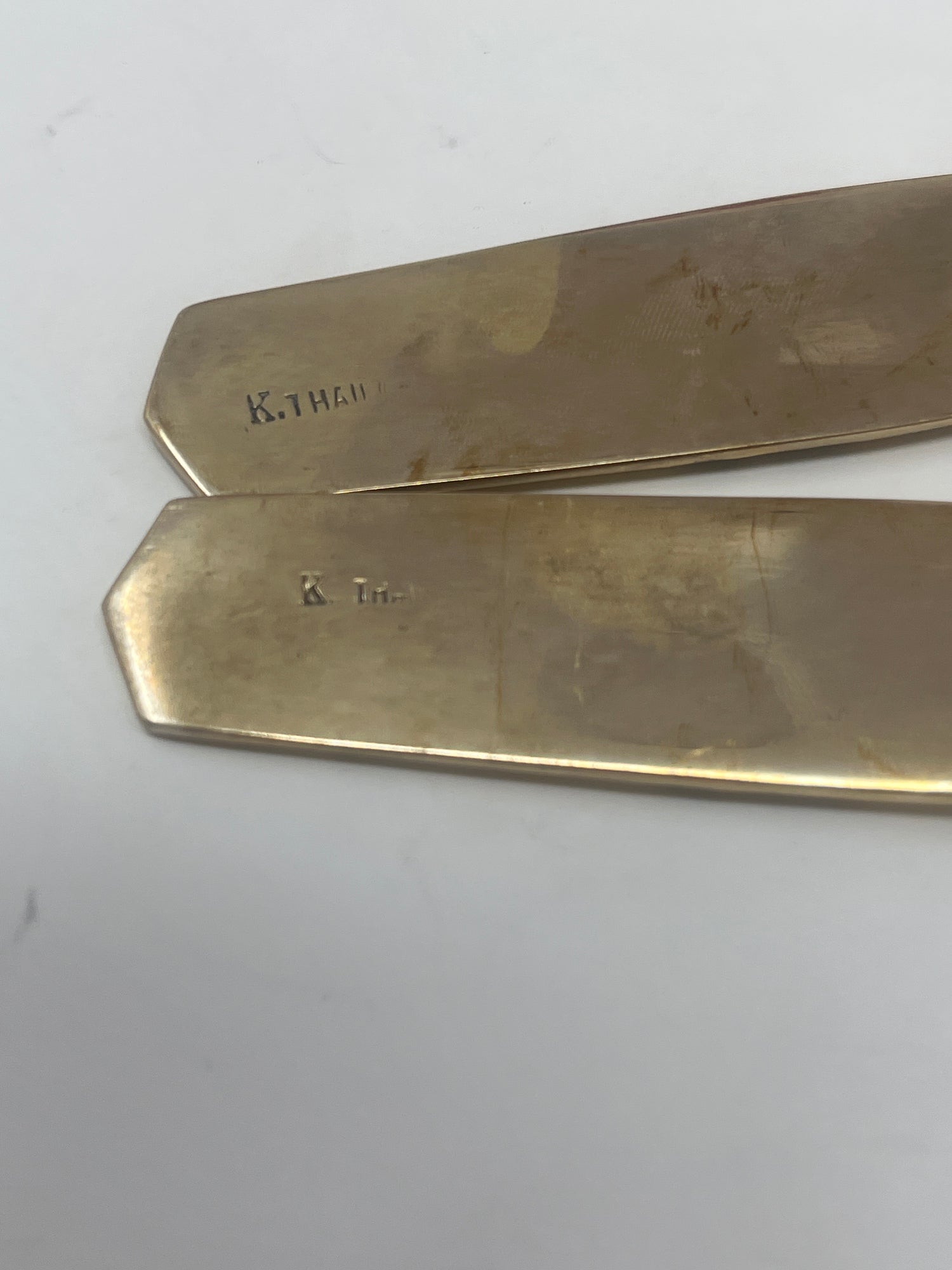 Thai brass serving fork and spoon set with embossed handle design, elegantly displayed on a smooth surface, highlighting their refined craftsmanship and functionality.