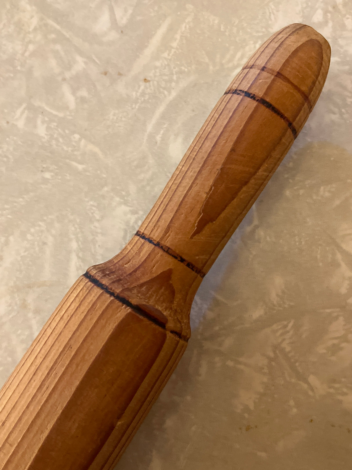 Wooden belan rolling pin's handle end on a textured countertop, showcasing its smooth, lathe-turned French-style design, ideal for precise dough rolling.