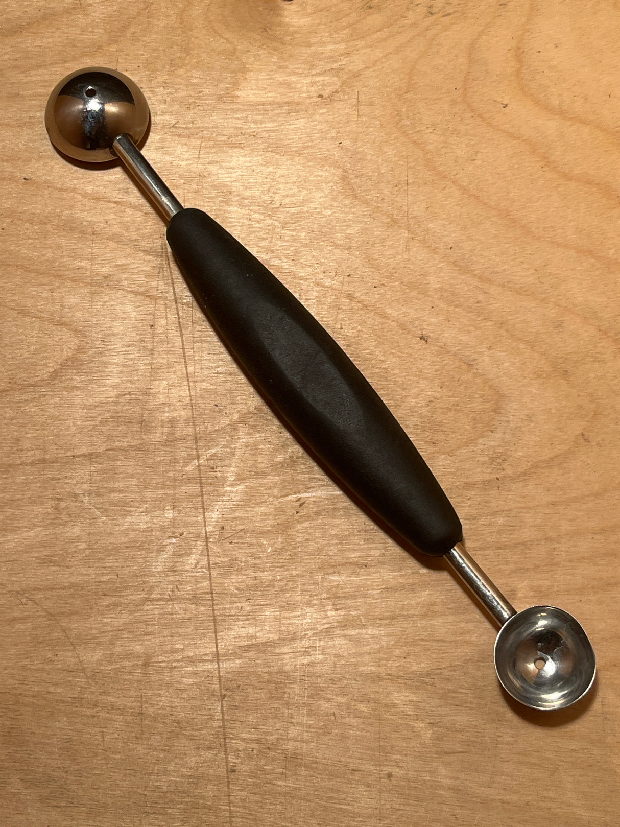 Melon baller with silicone handle - OXO Good Grips, featuring dual scoops for varied sizes on a wooden surface, ideal for creating perfect melon balls with ease.