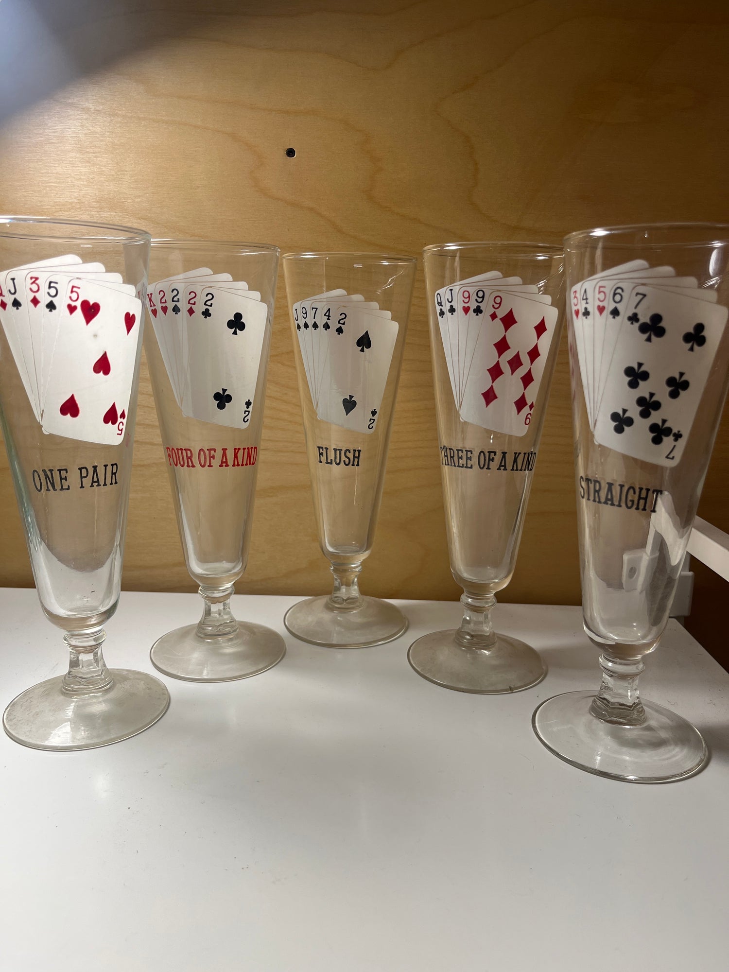 RARE 1960’s MCM poker-themed drinkware set featuring five tall glasses, each with a unique poker hand design: One Pair, Four of a Kind, Flush, Three of a Kind, Straight.