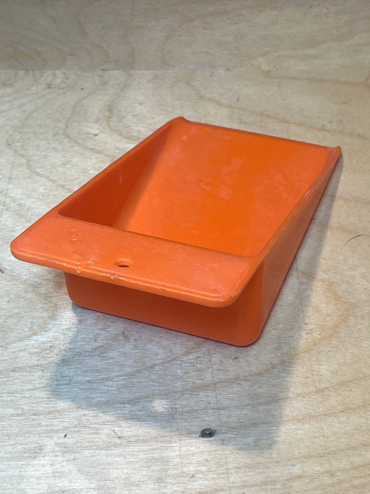 Orange pantry scoop - vintage plastic Tupperware with a flanged lip and handle, ideal for scooping pantry essentials, shown on a plywood surface.