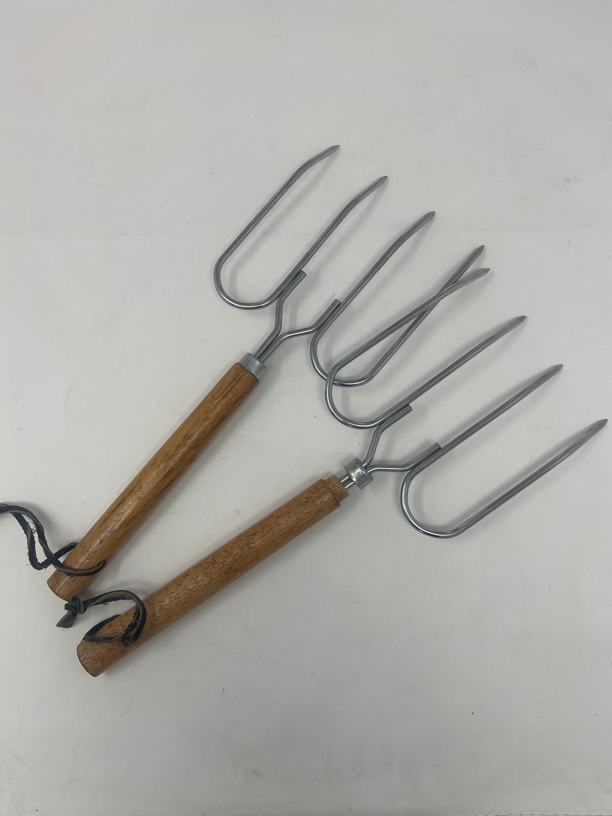 Set of two vintage roast forks with wooden handles, ideal for grilling meats and whole vegetables, showcased among other tools and kitchen utensils.