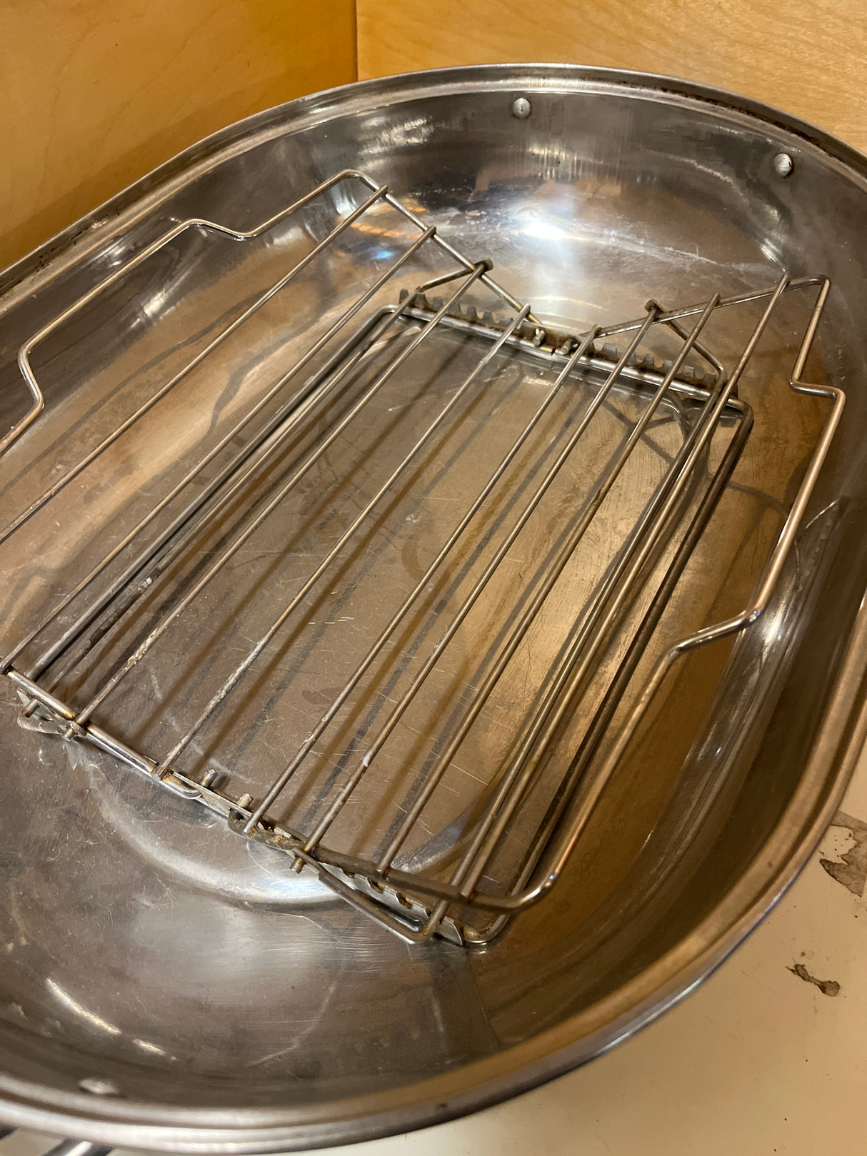 Stainless steel oval roasting pan with rack and lid, featuring a detachable wire rack inside, ideal for roasting meats or vegetables, collecting drippings efficiently.