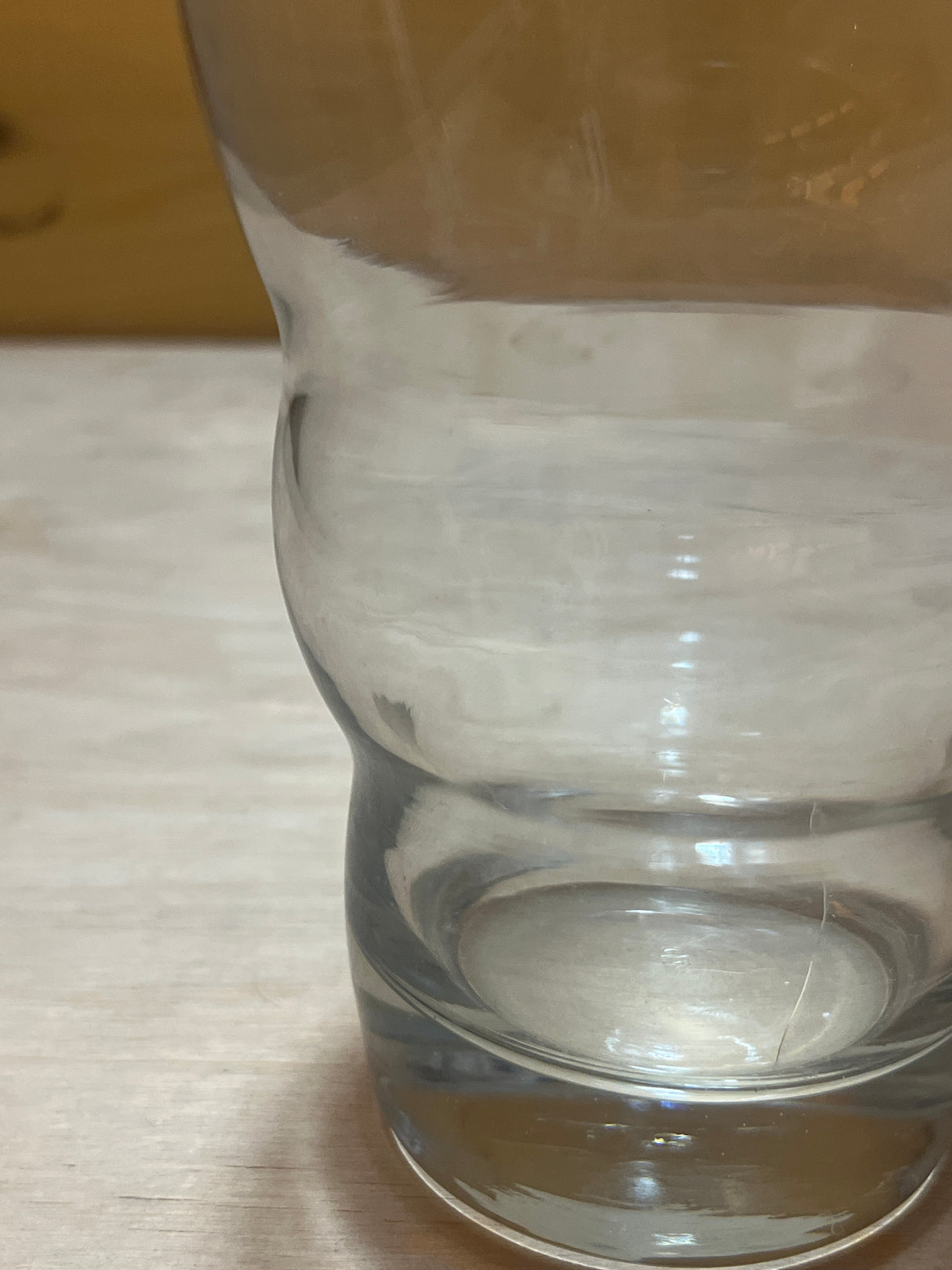 Wavy sided tall drinking glass on a wooden surface, showcasing its unique undulating design and clear structure.