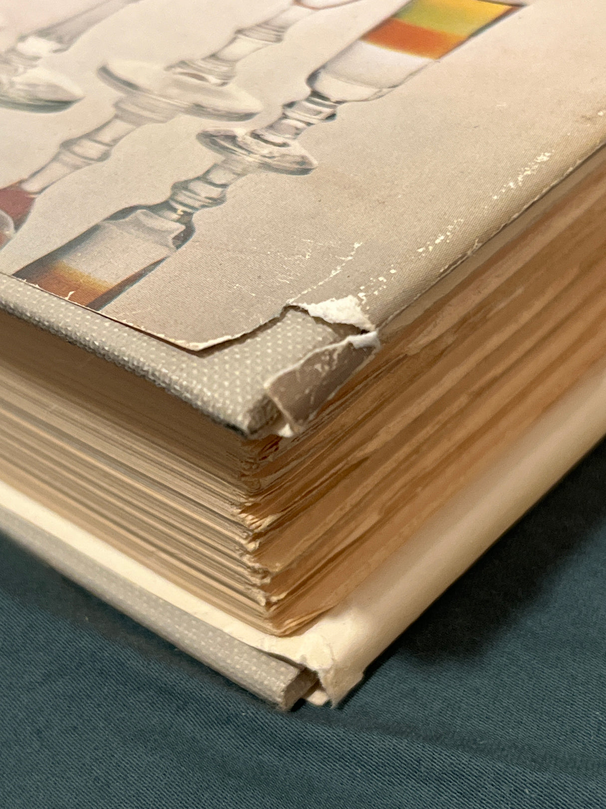 Trader Vic’s Bartender’s Guide (Revised 1972) hardcover with deckled edges, shows peeling cloth cover at corner, revealing board underneath, featuring glassware design.