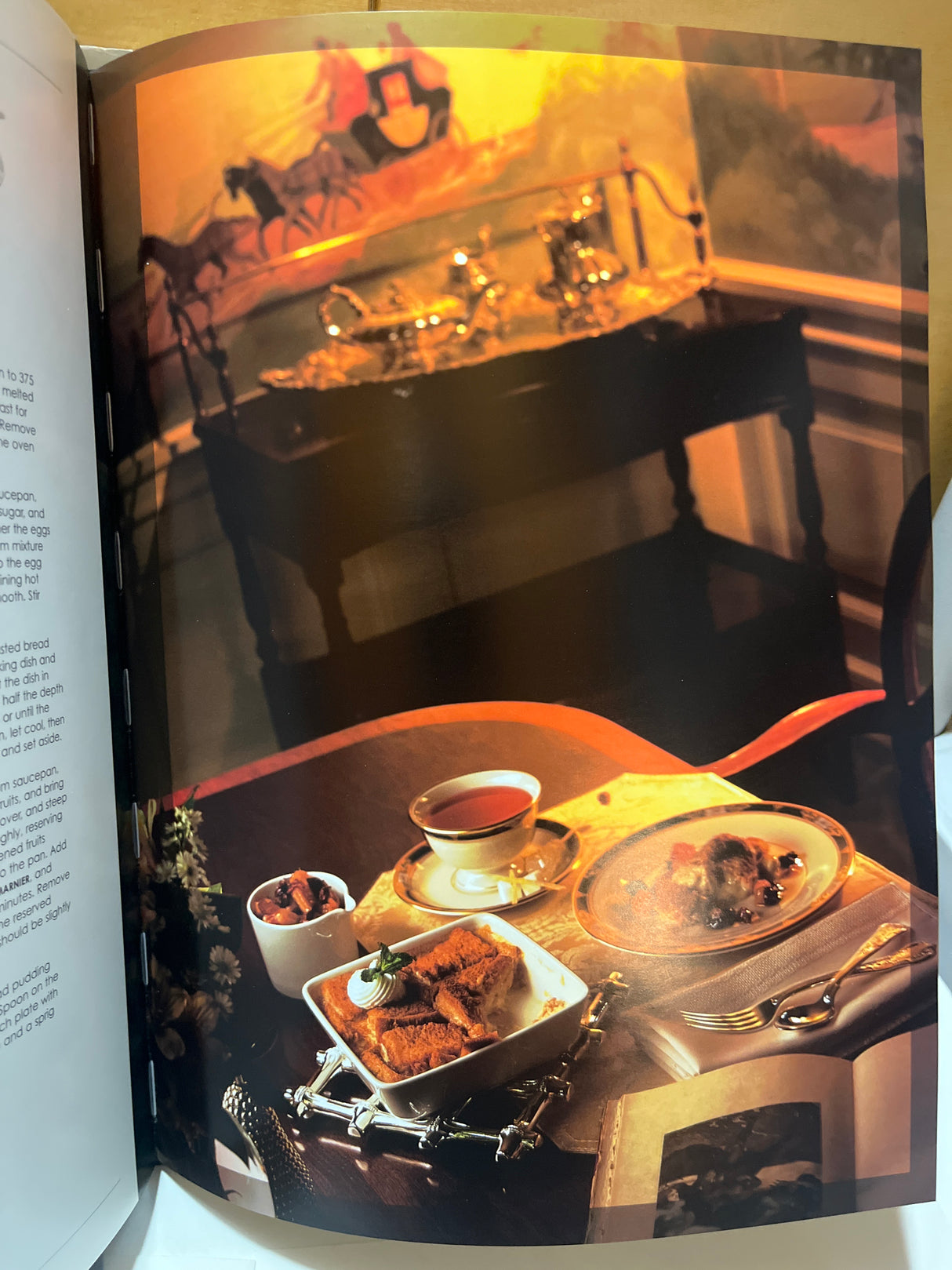 RARE Duquesne Club Cookbook: A square ceramic dish with bread pudding, whipped cream, mint, alongside a ramekin of fruit, set on an old-world dining table.