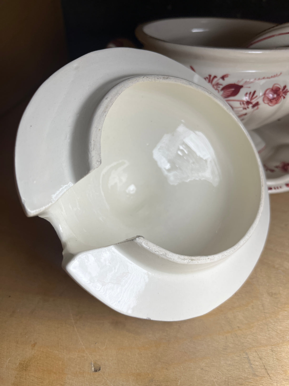 Porcelain soup tureen bowl with lid, underplate, and ladle, hand-painted with red roses, displayed on a wood shelf; note minor chips on the rim.