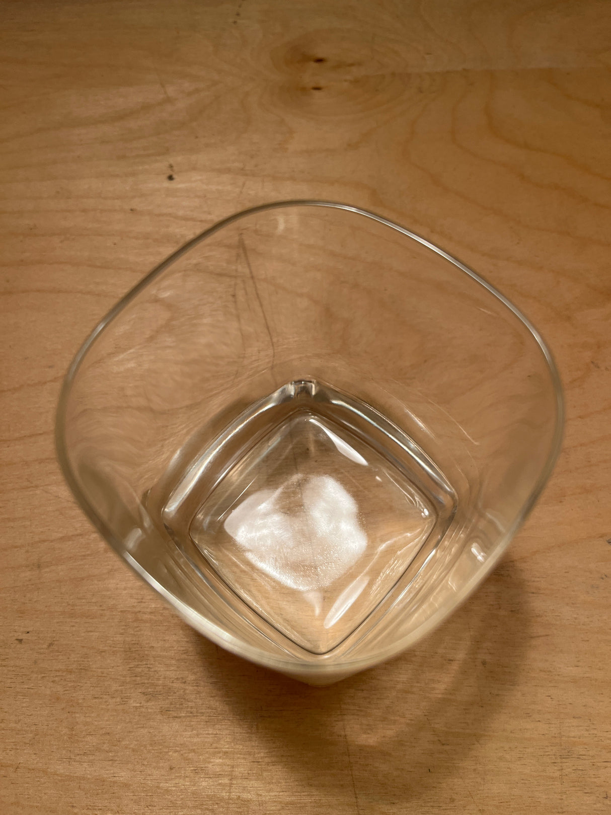 Square heavy bottom tumbler drinking glass on a wooden surface, showcasing its clear, square design and robust base, with light reflections hinting at subtle elegance.