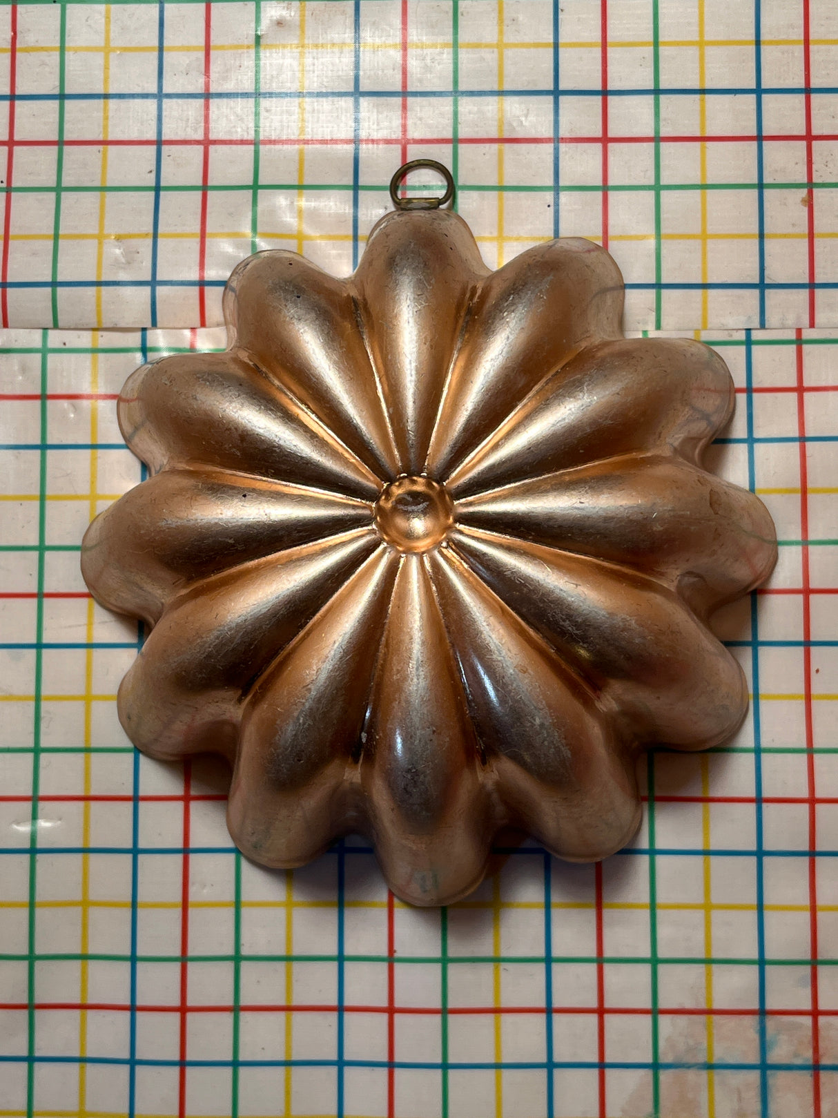 Copper-lined aluminum mold for jello, shaped like a multi-petaled flower, with a small hanging ring at the top for easy display.