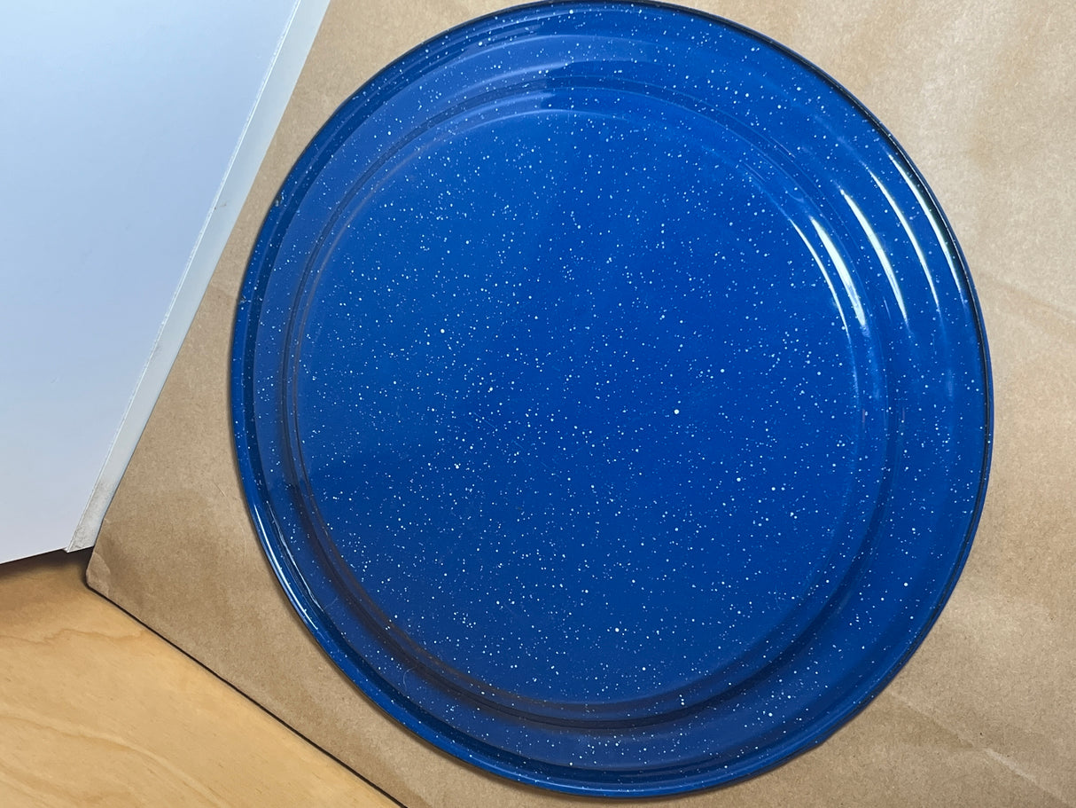 Blue speckled enamelware plate on kraft-paper surface, showcasing its lightweight, durable build, ideal for outdoor activities like cookouts or camping.