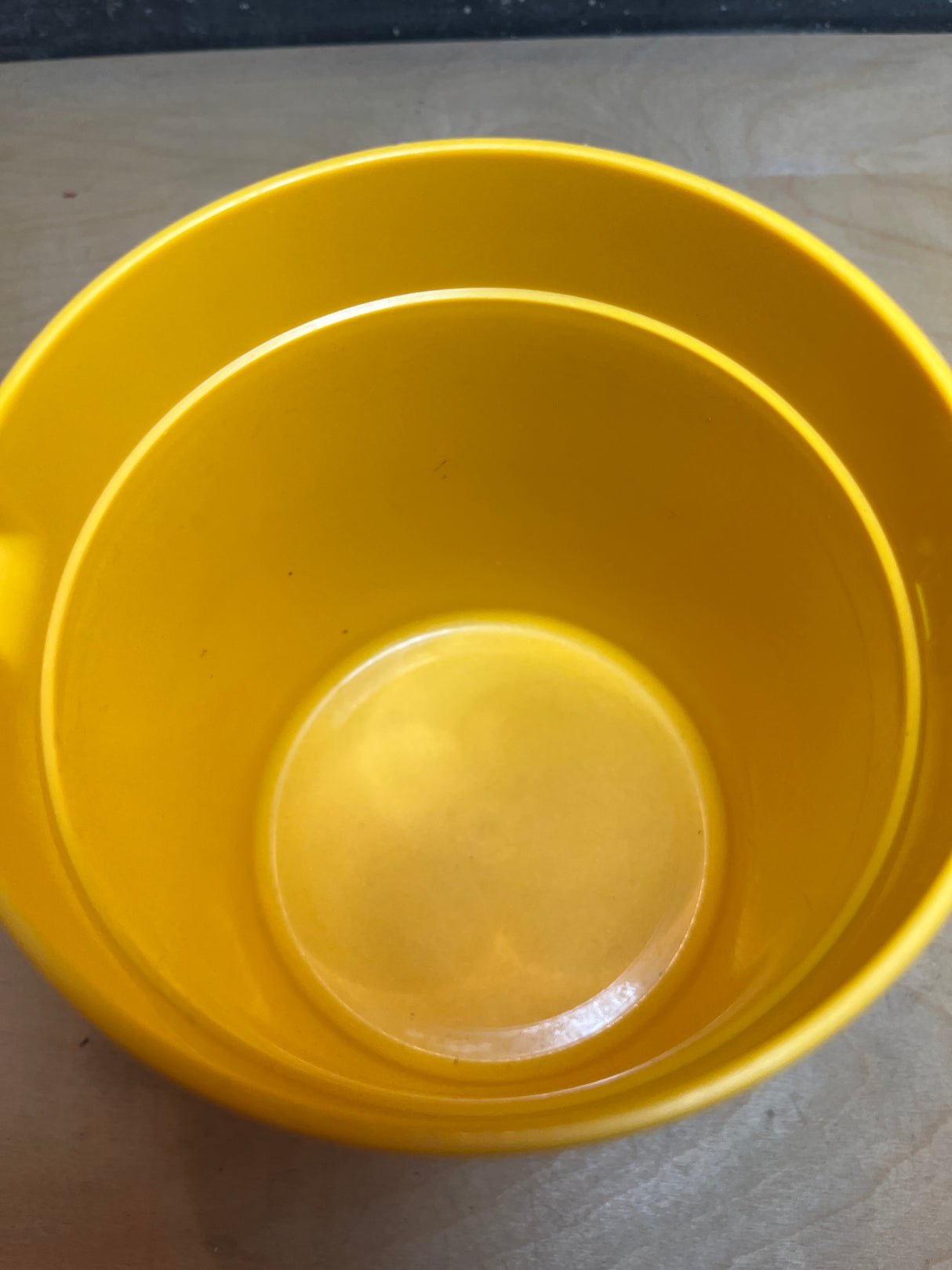 Tupperware golden yellow pitcher, empty and viewed from above, resembles a small bucket-style container on a light wood surface.