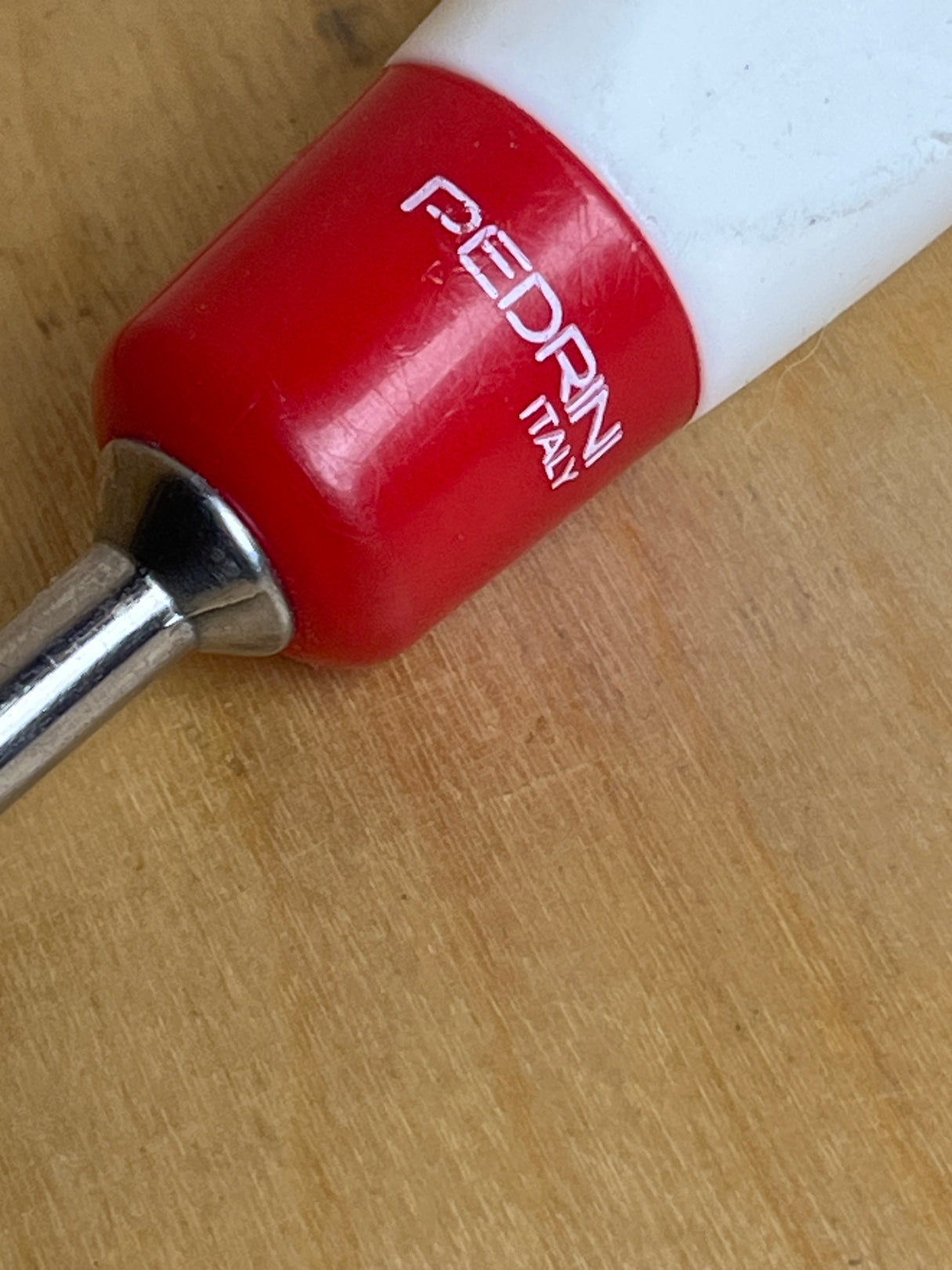 Close-up of Pedrini stainless steel slotted serving spoon handle, showcasing the red and white grip with PEDRINI ITALY stamped, attached to a metal shaft.