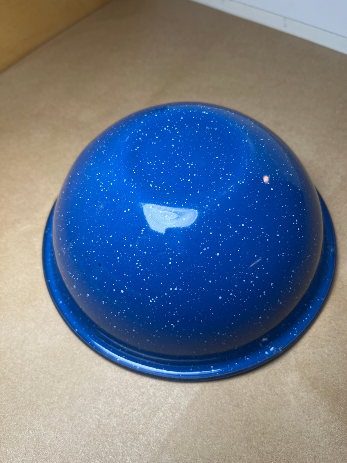 Blue speckled enamelware bowl, glossy with white flecks, turned upside-down on a countertop. Lightweight and durable, ideal for cookouts or camping.
